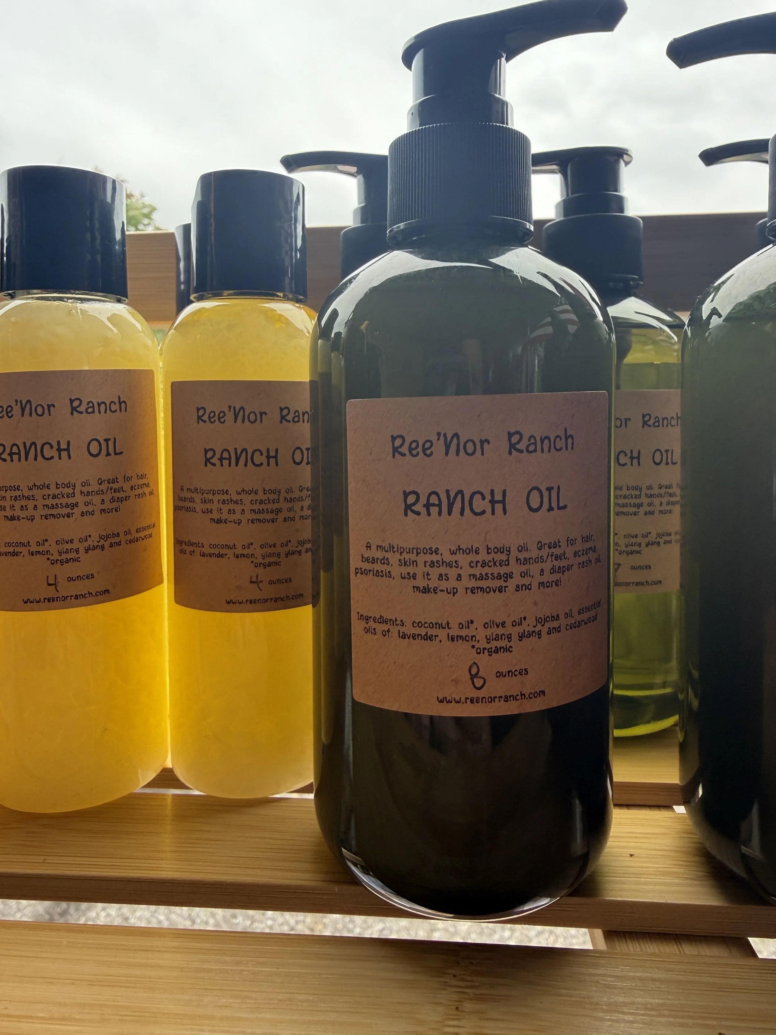 Pump bottles of Ree'nor Ranch ranch oil with beige labels on a wooden shelf