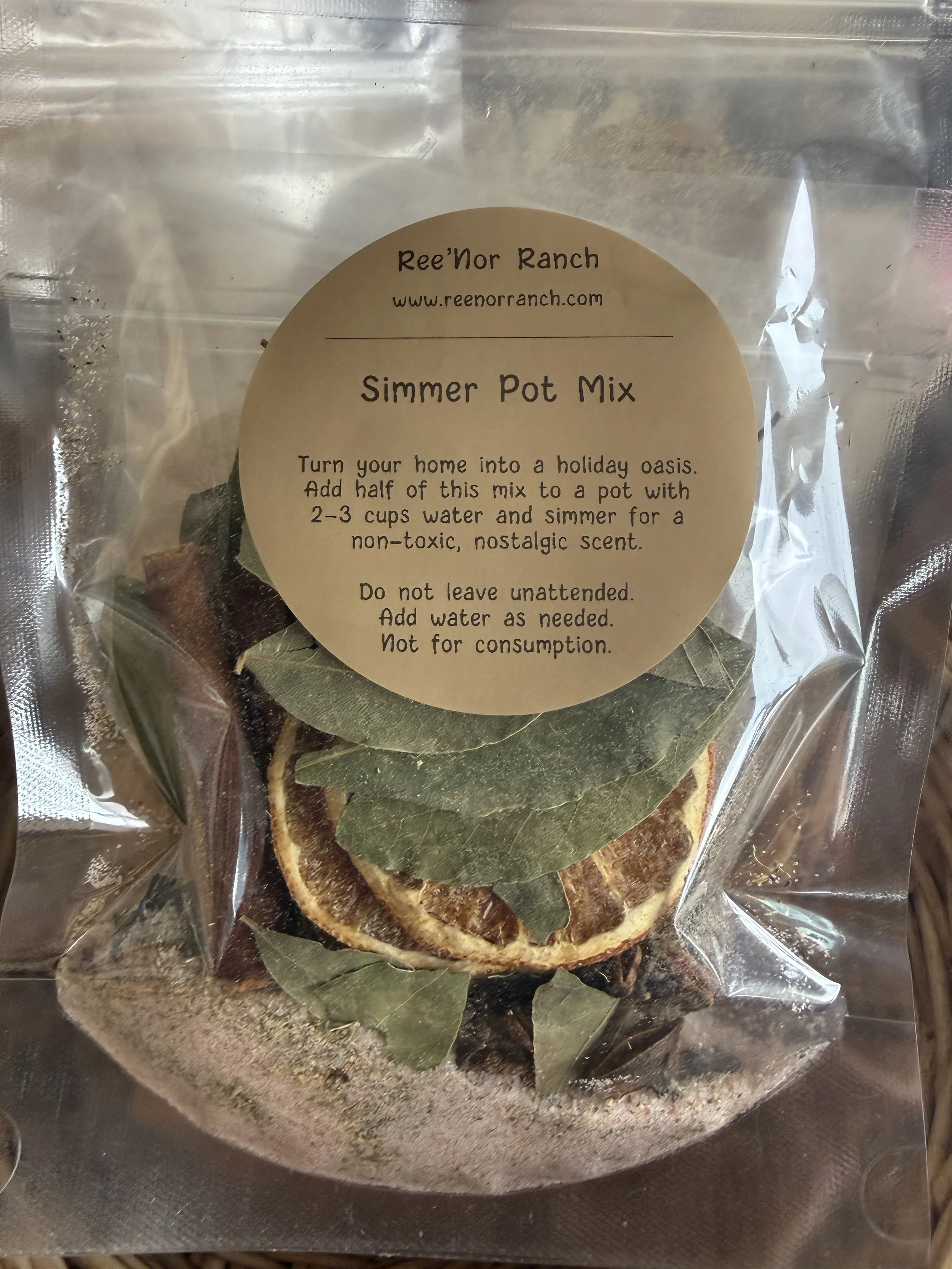 A clear plastic bag containing dried citrus slices and bay leaves labeled 'Simmer Pot Mix' from Ree'r Ranch. The label includes instructions for use and the website www.reenorranch.com.