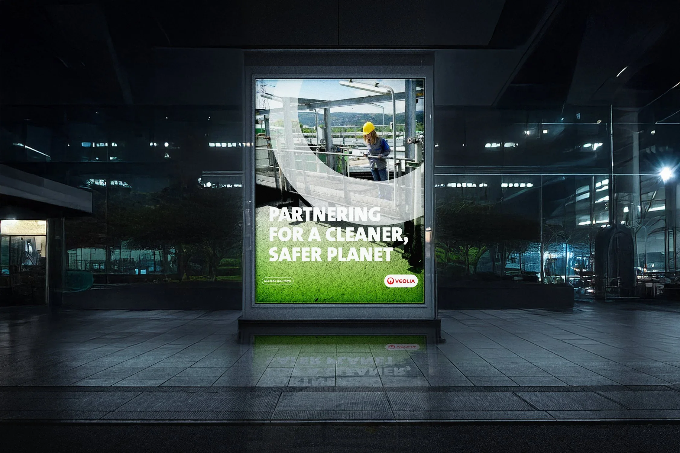 Digital billboard with an environmental campaign message that reads 'Partnering for a cleaner, safer planet' and features a worker in a safety helmet on an industrial site, with reflections on the surrounding building windows.
