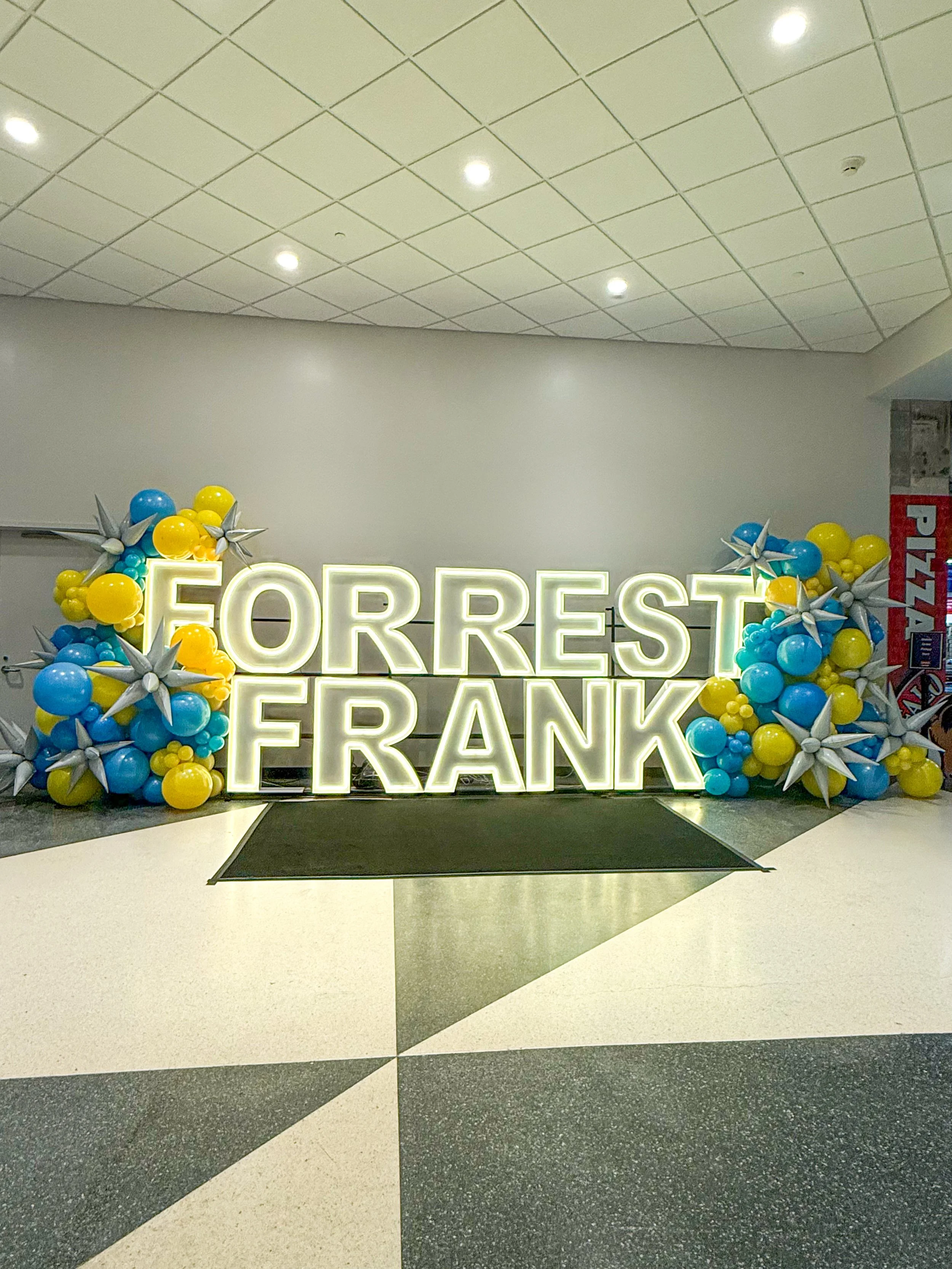 LED marquees spelling Forrest Frank with blue and yellow balloons and white starburst