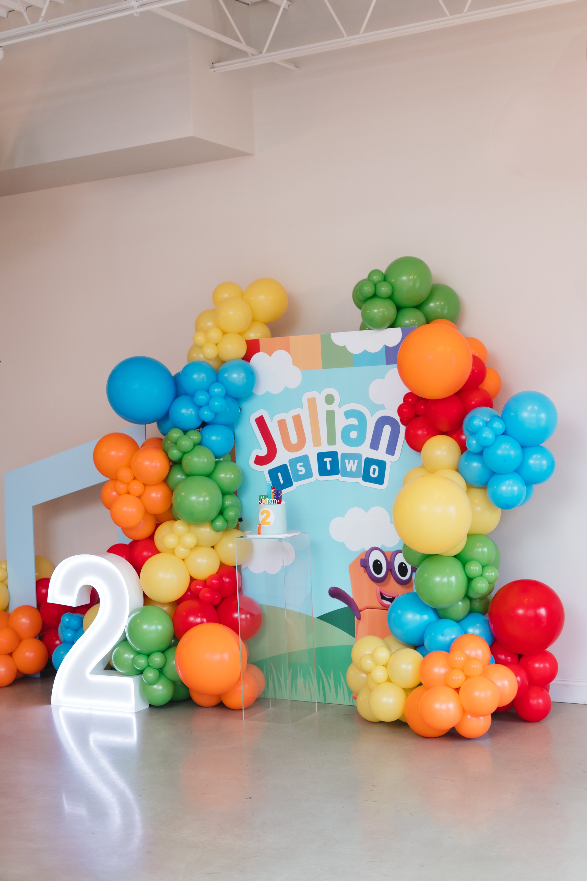 Colorful birthday decorations with balloons and a large number one, a sign that says "Julian is One Happy Dude" for a first birthday celebration.
