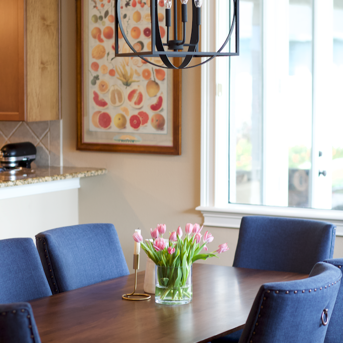Dining room table with bold, blue chairs, an iron light fixture above, and a bouquet of tulips.