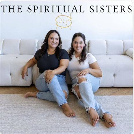 Two women sitting on the floor in front of a white couch, smiling, with the text "The Spiritual Sisters" and a gold logo above them.