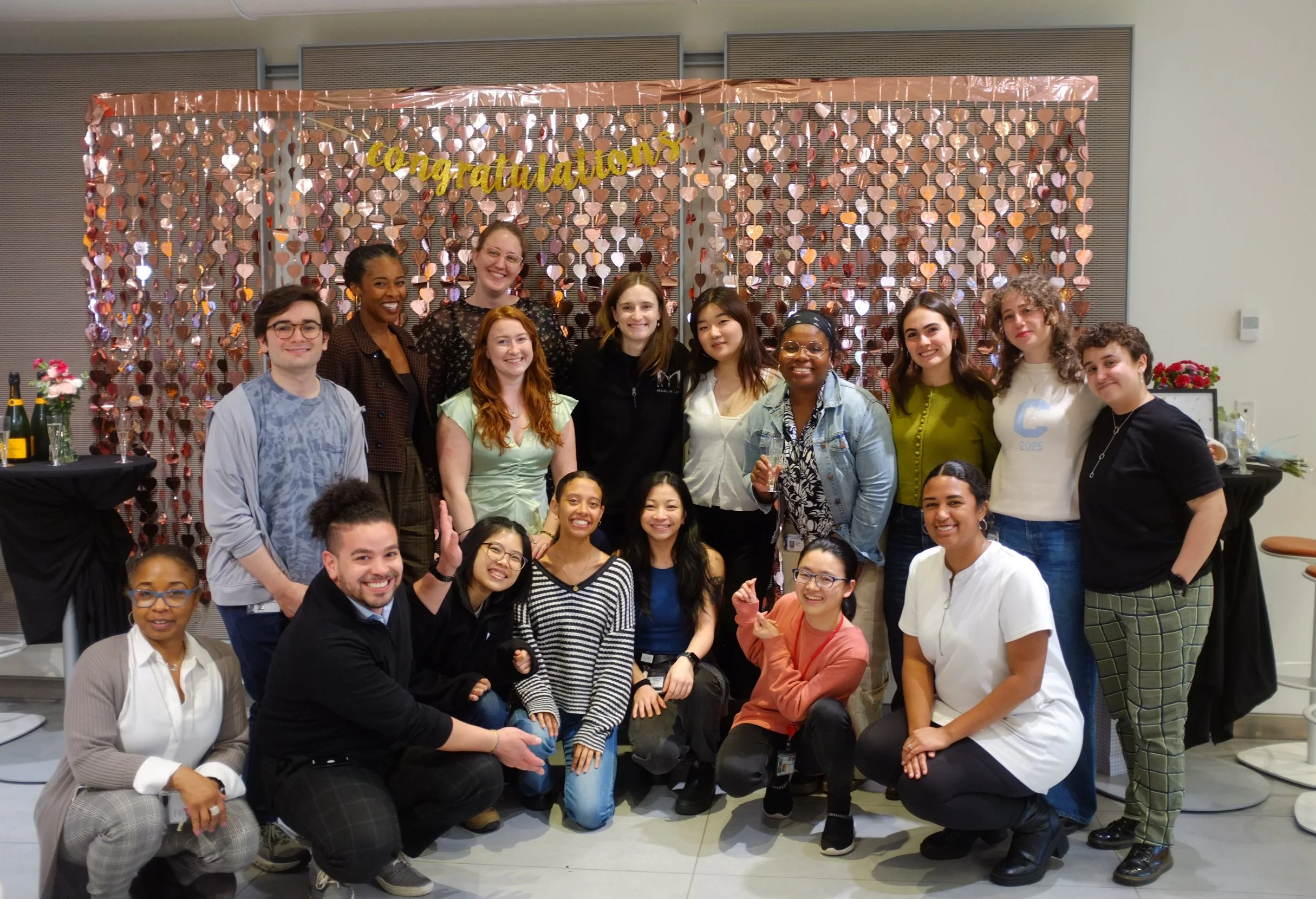 Group of people posing in front of a decorative backdrop with a 'Congratulations' banner at an indoor celebration.