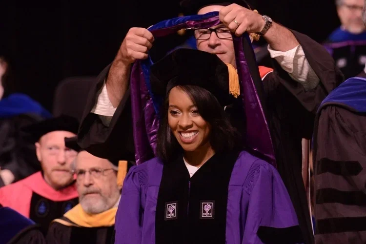 Dr. Jones Marlin dressed in doctoral graduation robes while receiving dissertation a prize