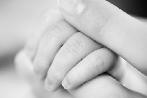 A baby's hand between an adults fingers