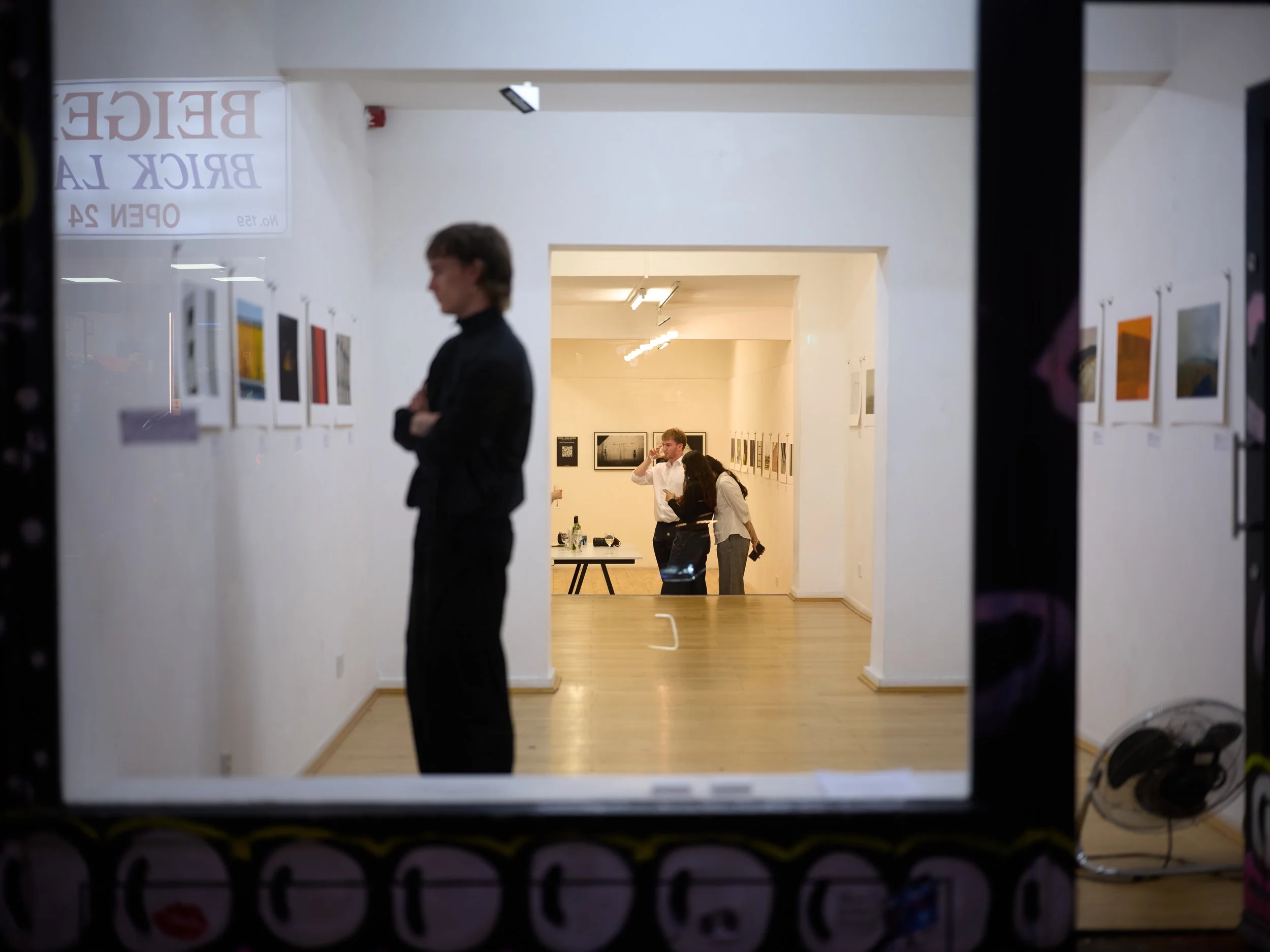 View through the window of The Brick Lane Gallery showing guests at the opening night of the exhibition The World Is Colourful in London