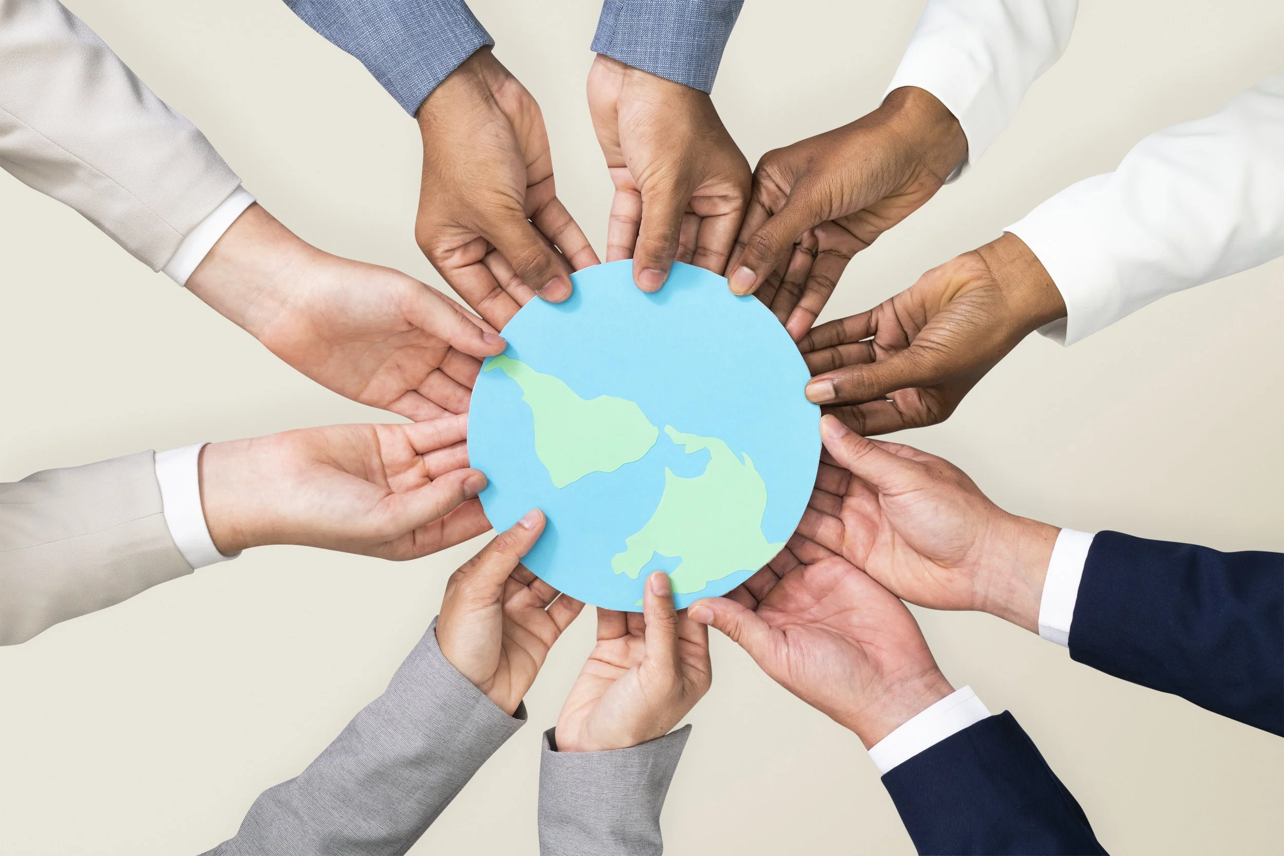 Hands from diverse races hold a paper globe in a circle together