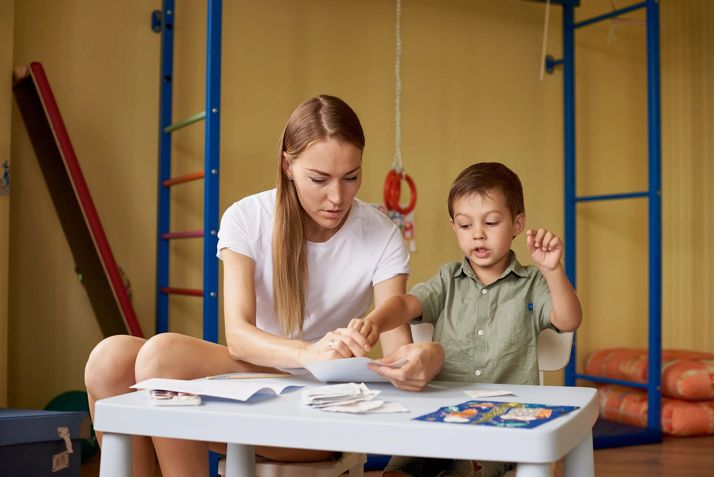 Adult and child sit at a table using flash cards in a therapy or learning room.