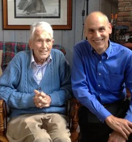A photo of Dr. Cooke, an elderly man in a blue cardigan sweater, and the interviewer.