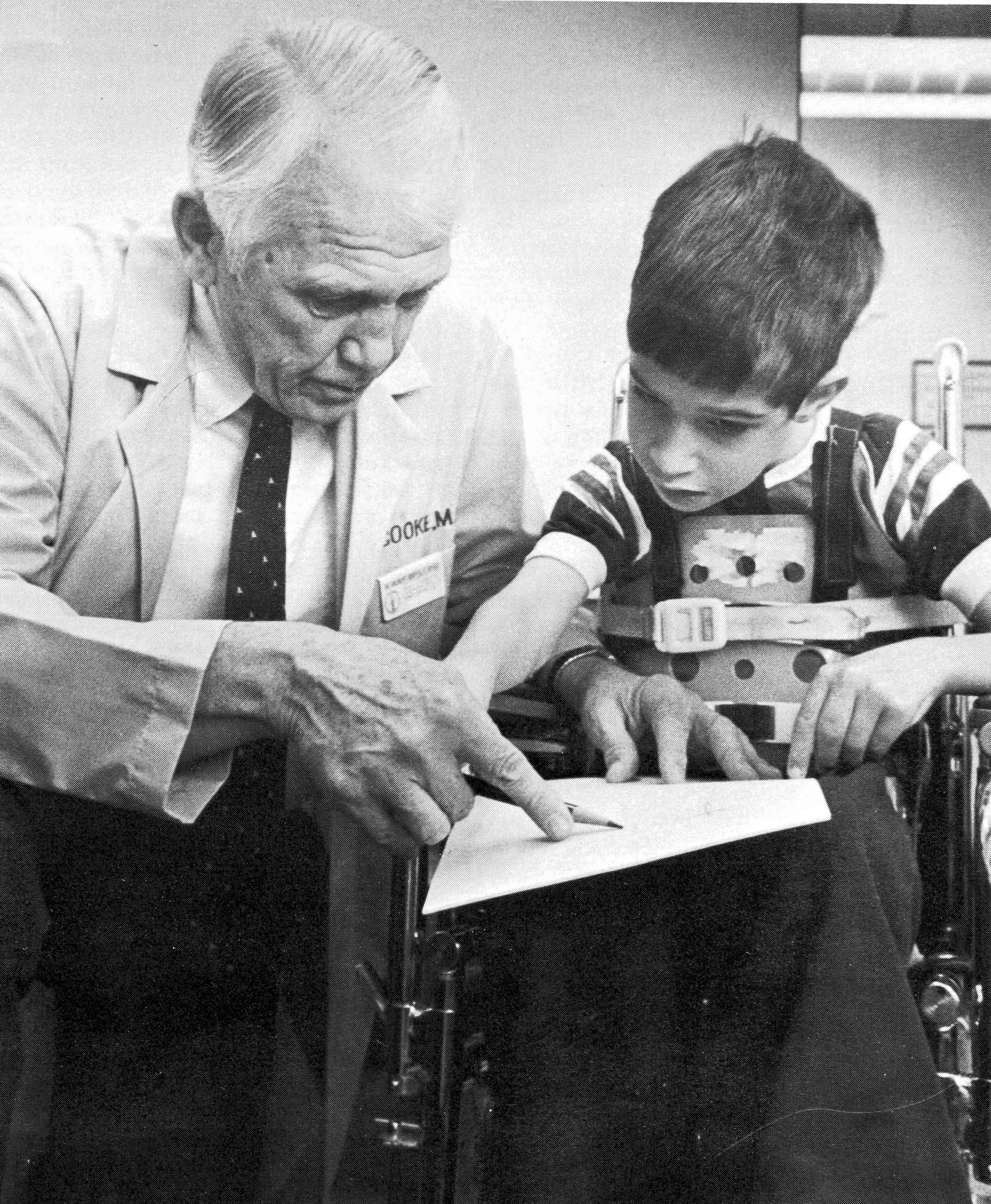 An older photo of Dr. Cooke in clinic, working with a little boy who is wheelchair bound.