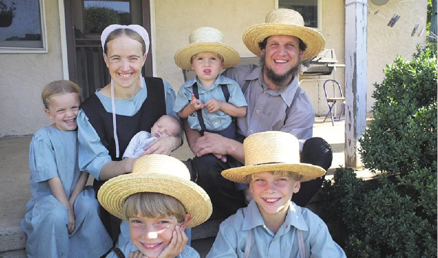 An amish couple sit on their front porch surrounded by their 5 children