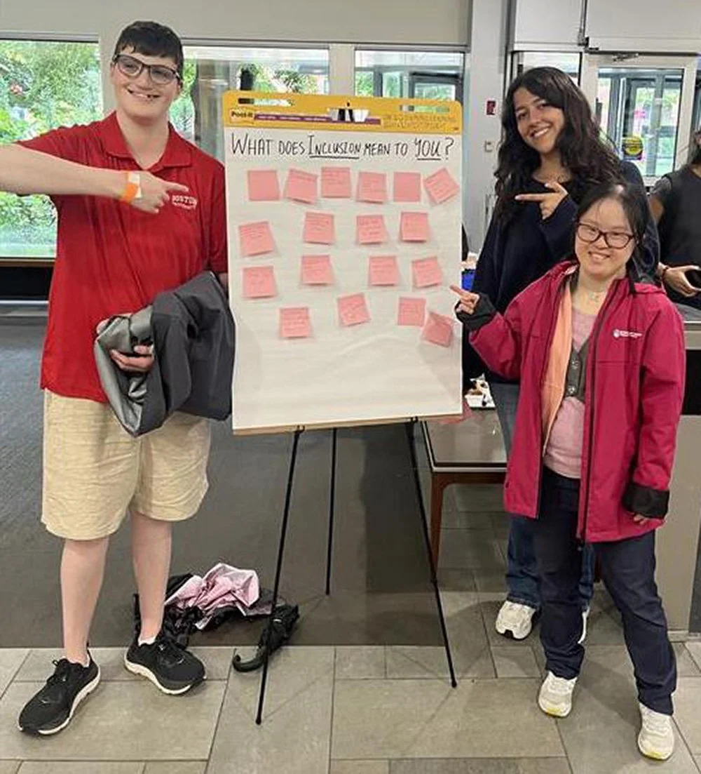 3 researchers standing with a giant tablet that says "What does inclusion mean to you?" The tablet is covered in responses written on post-it notes.