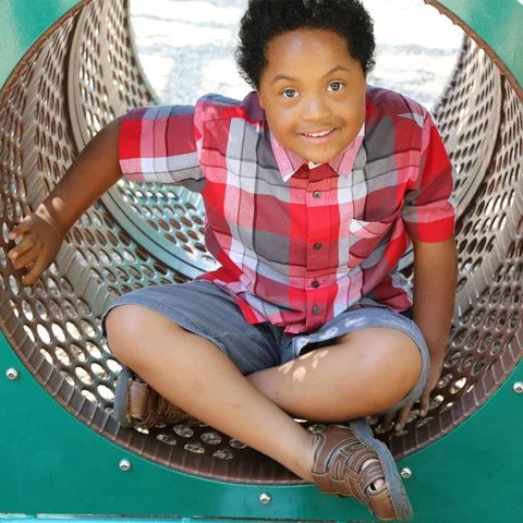 A young boy with Down syndrome smiles as he plays on playground equipment