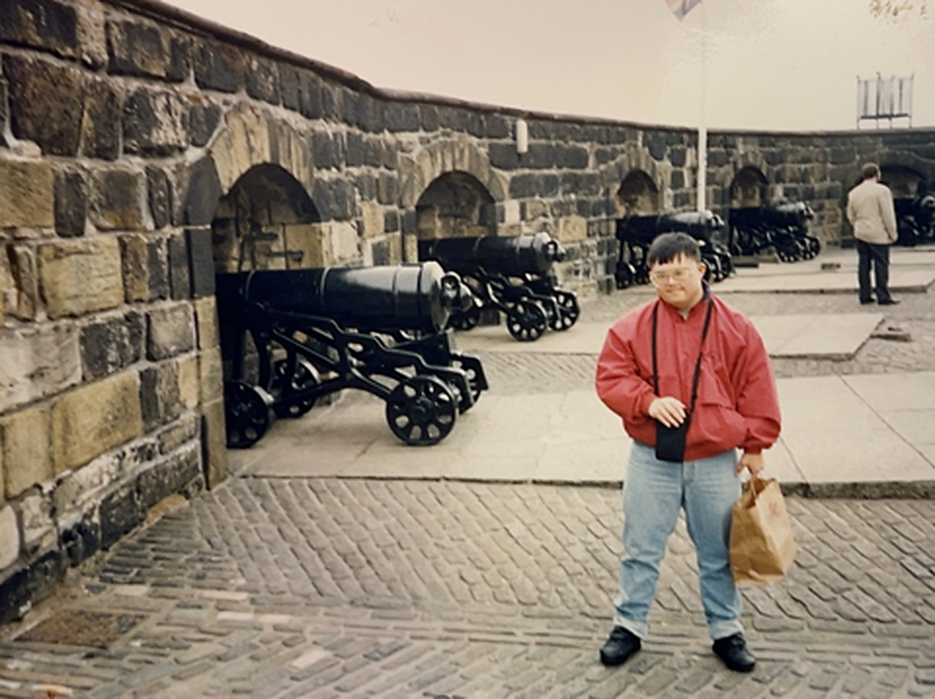 A young Koji on vacation at a fortress with cannons and a rock wall in the background