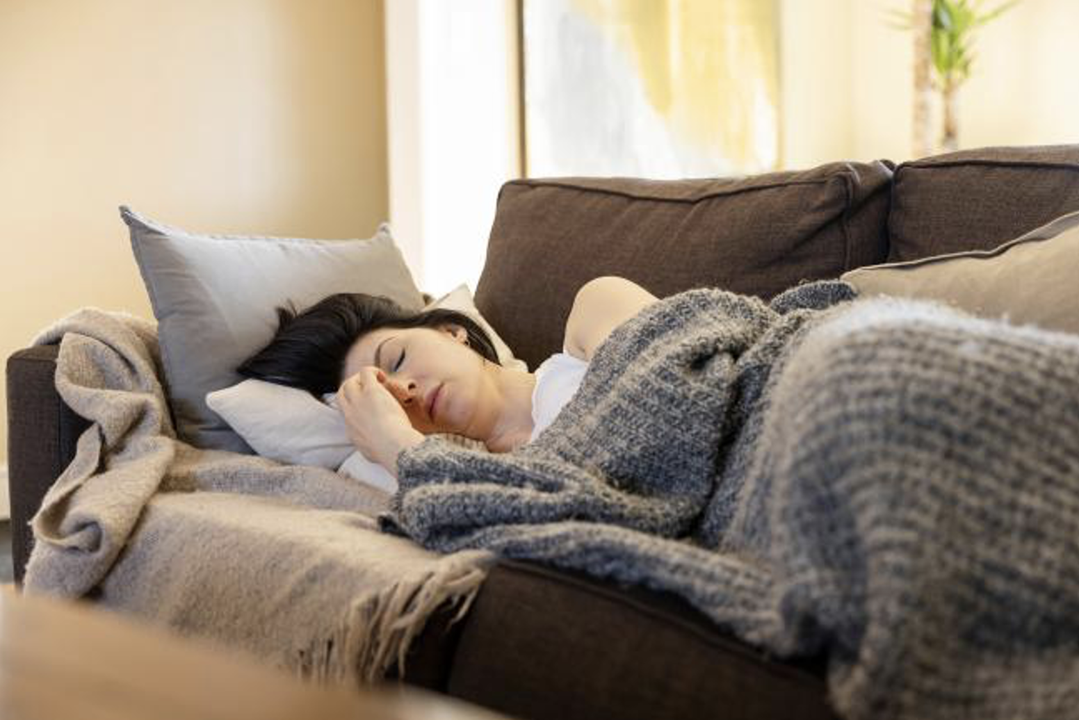 A sick woman lies on a couch, wincing from headache pain