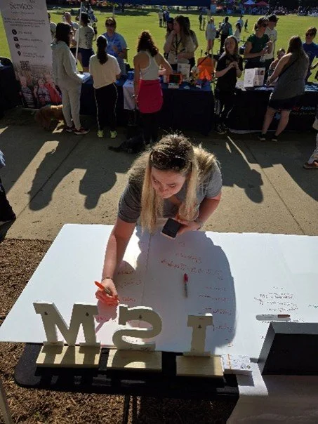 A woman participates by writing a word she associates with autism on poster board.