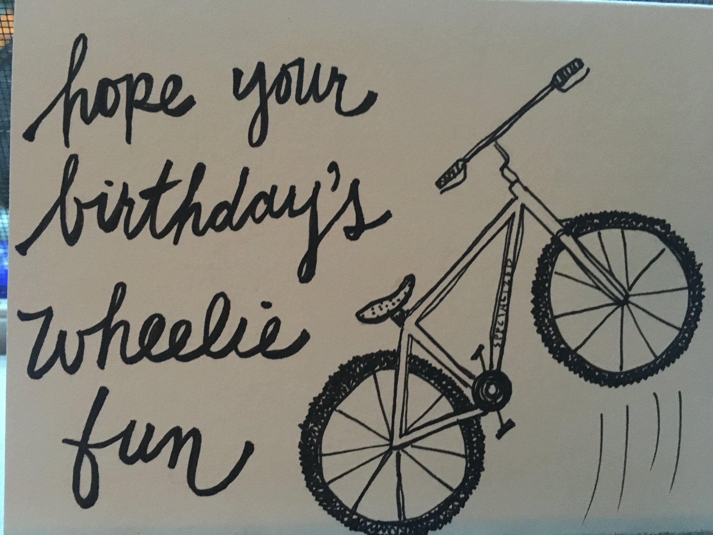 a doodle of a mountain bike doing a wheelie, with it's front tire being lifted, and the words "hope your birthday's wheelie fun" next to it; this was made for a friend who loves to mountain bike
