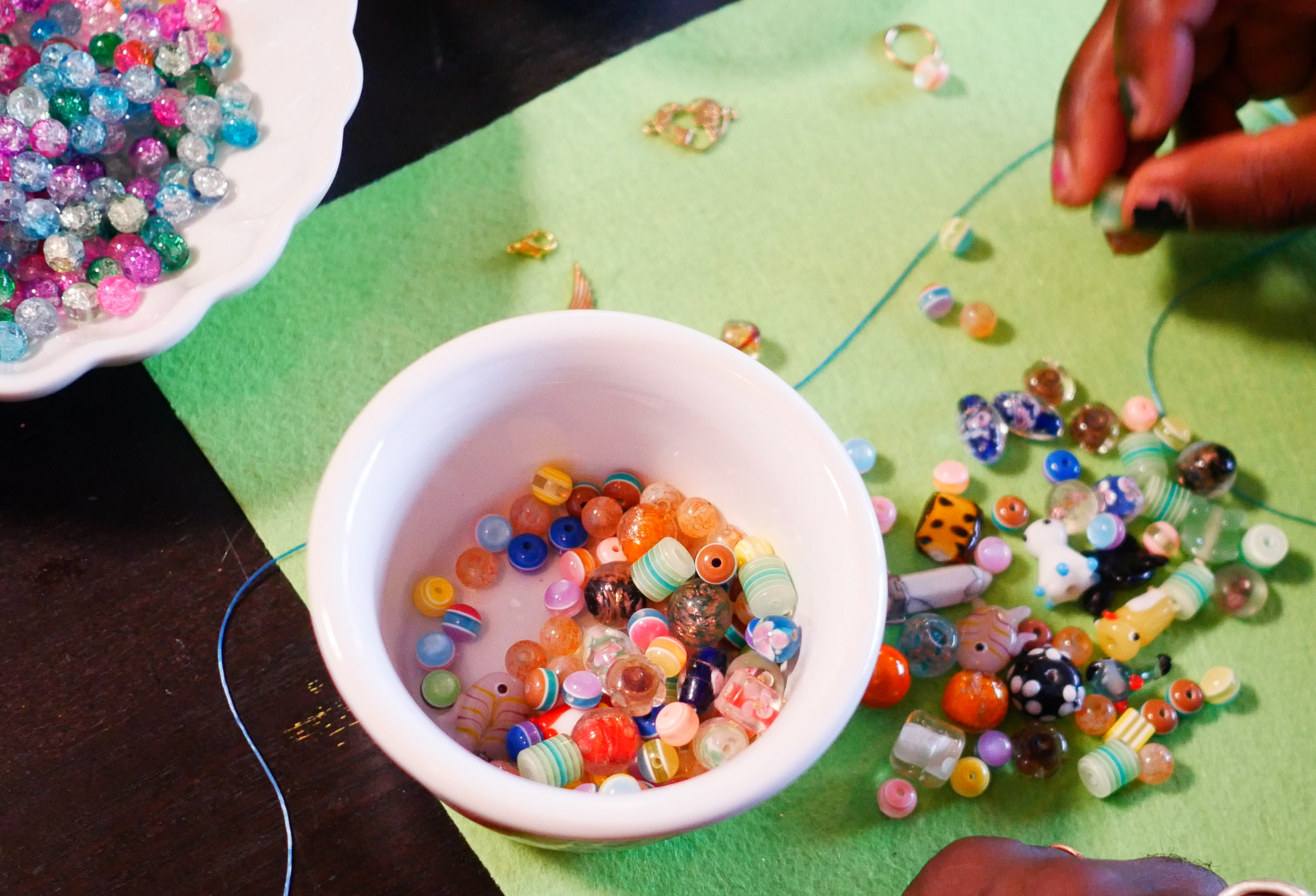 Hands stringing beads next to a bowl.