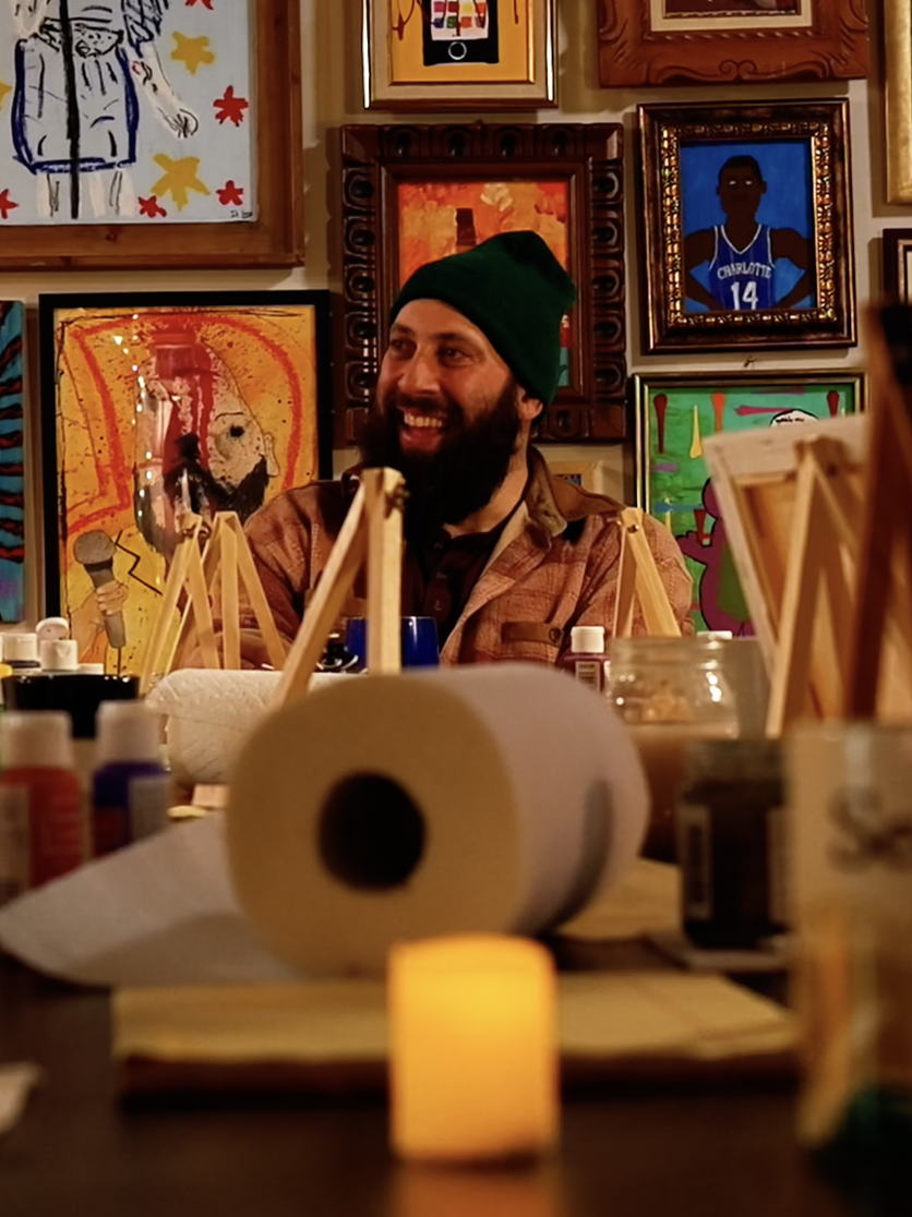 Dr Lemco sitting at a table laughing while painting.