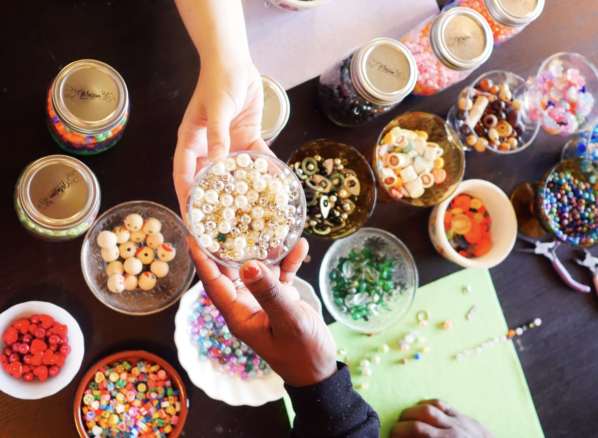 Hands handing a bowl of beads across the table