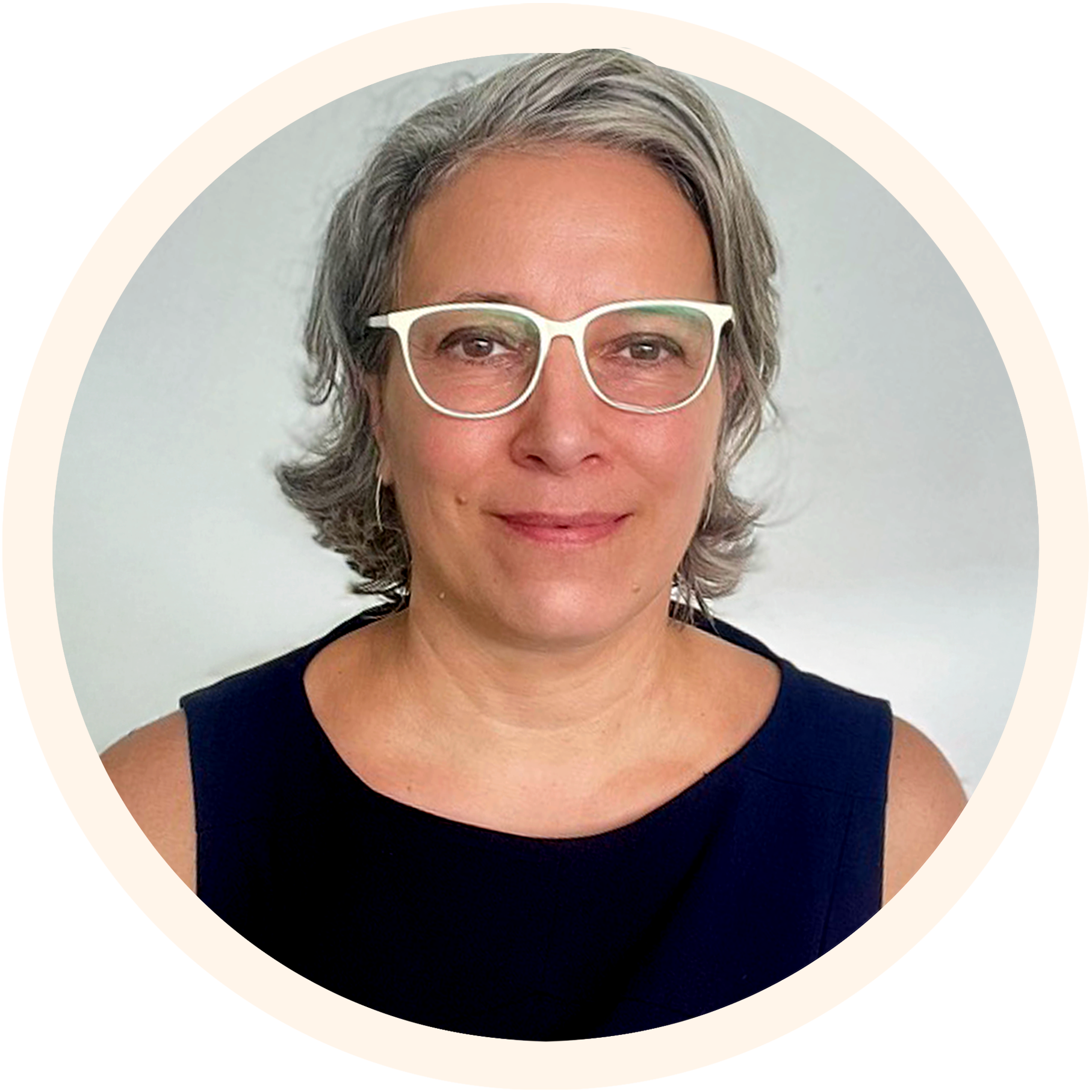 A woman with short gray hair, wearing white glasses and a navy sleeveless top, smiling at the camera, against a plain white background.