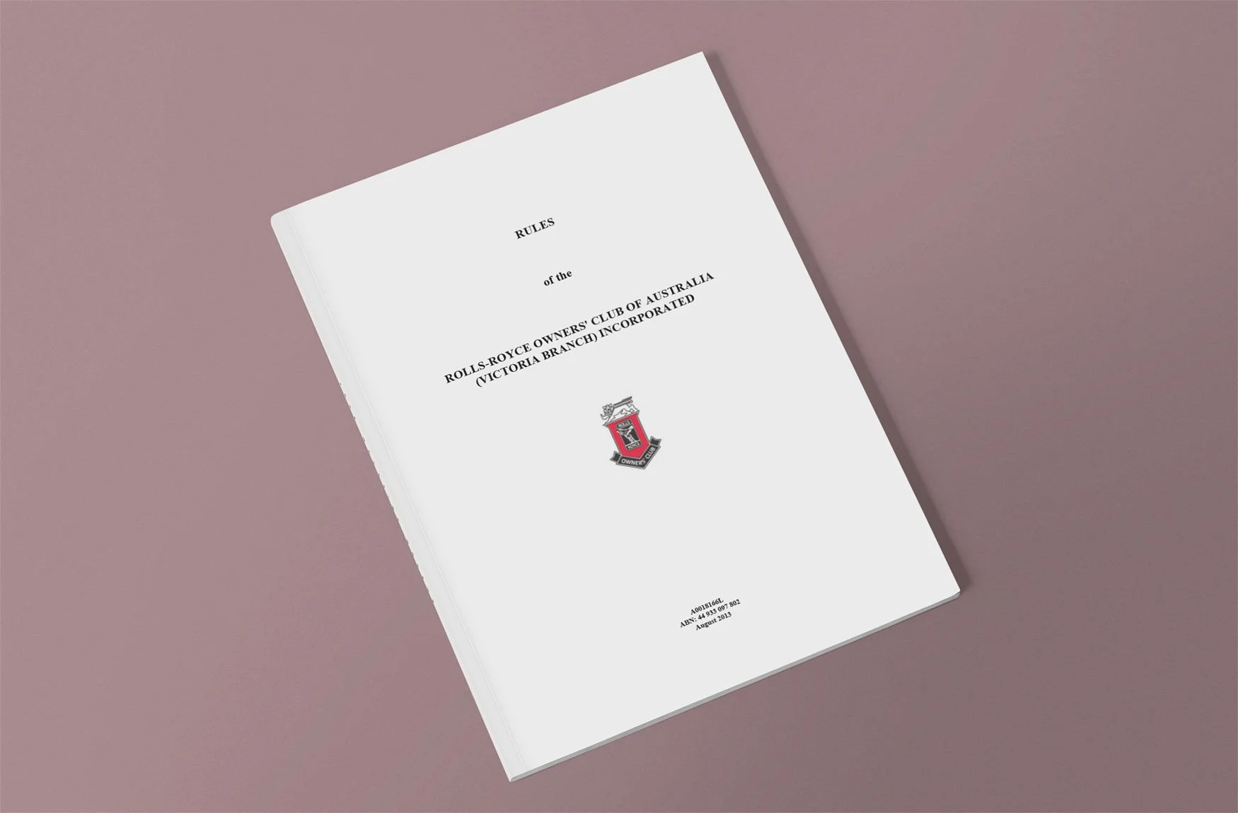 A white booklet titled 'Rules of the Rolls-Royce Owners' Club of Australia (Victoria Branch Incorporated)' with a logo featuring a shield and a crown, placed on a pinkish-brown surface.