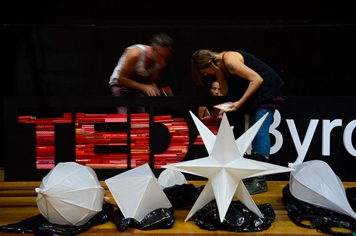 People setting up decorations and lighting for a TEDx event with large star-shaped ornaments and umbrellas on stage.