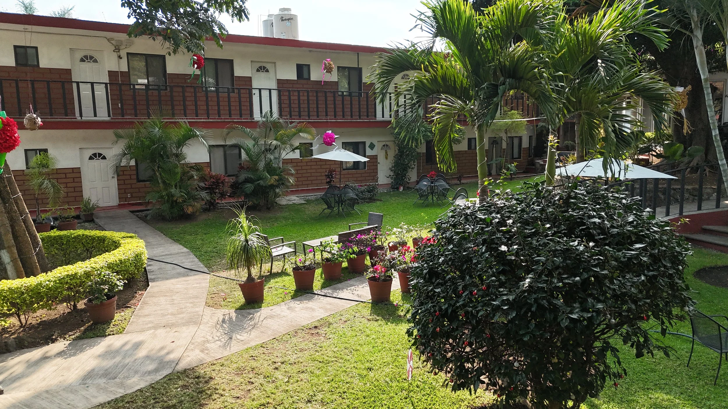 Jardín con mesas, sillas y plantas, en un complejo residencial.