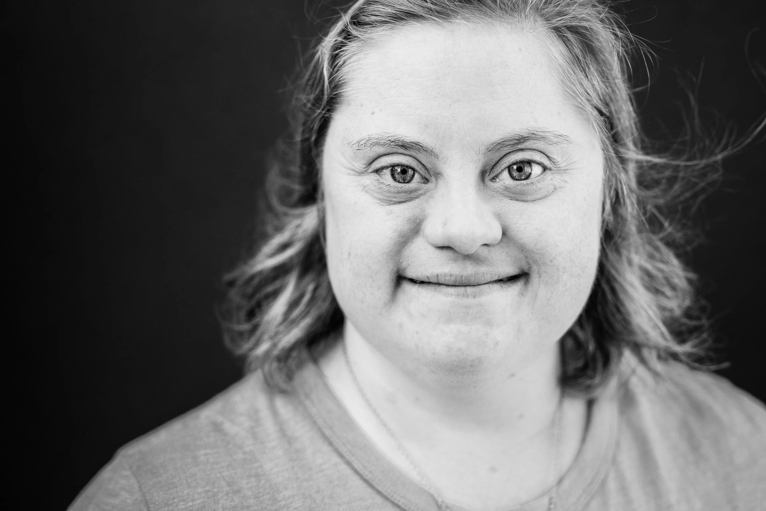 Black and white headshot of a GiGi's Playhouse NYC participant with down syndrome against a gray wall