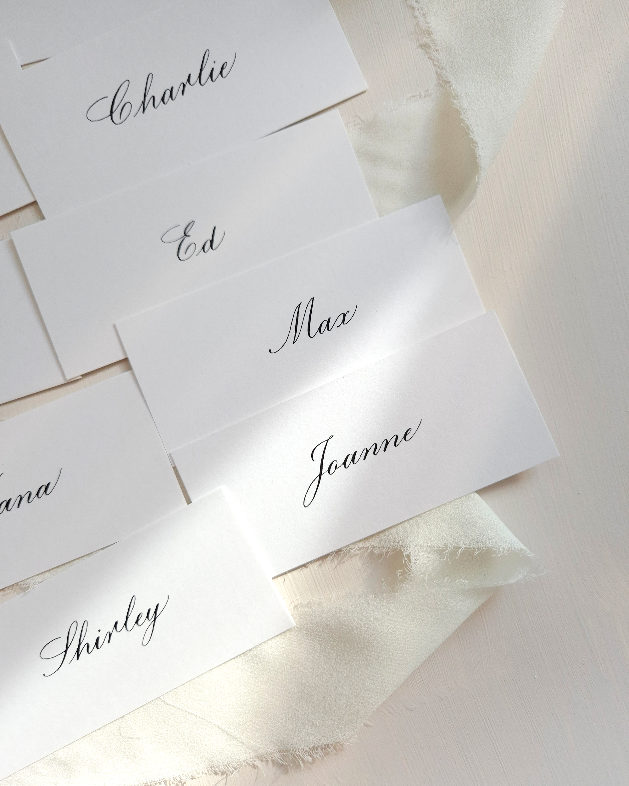 White place cards with black calligraphy writing. The names on the place cards are Charlie, Ed, Max, Joanne, and Shirley.