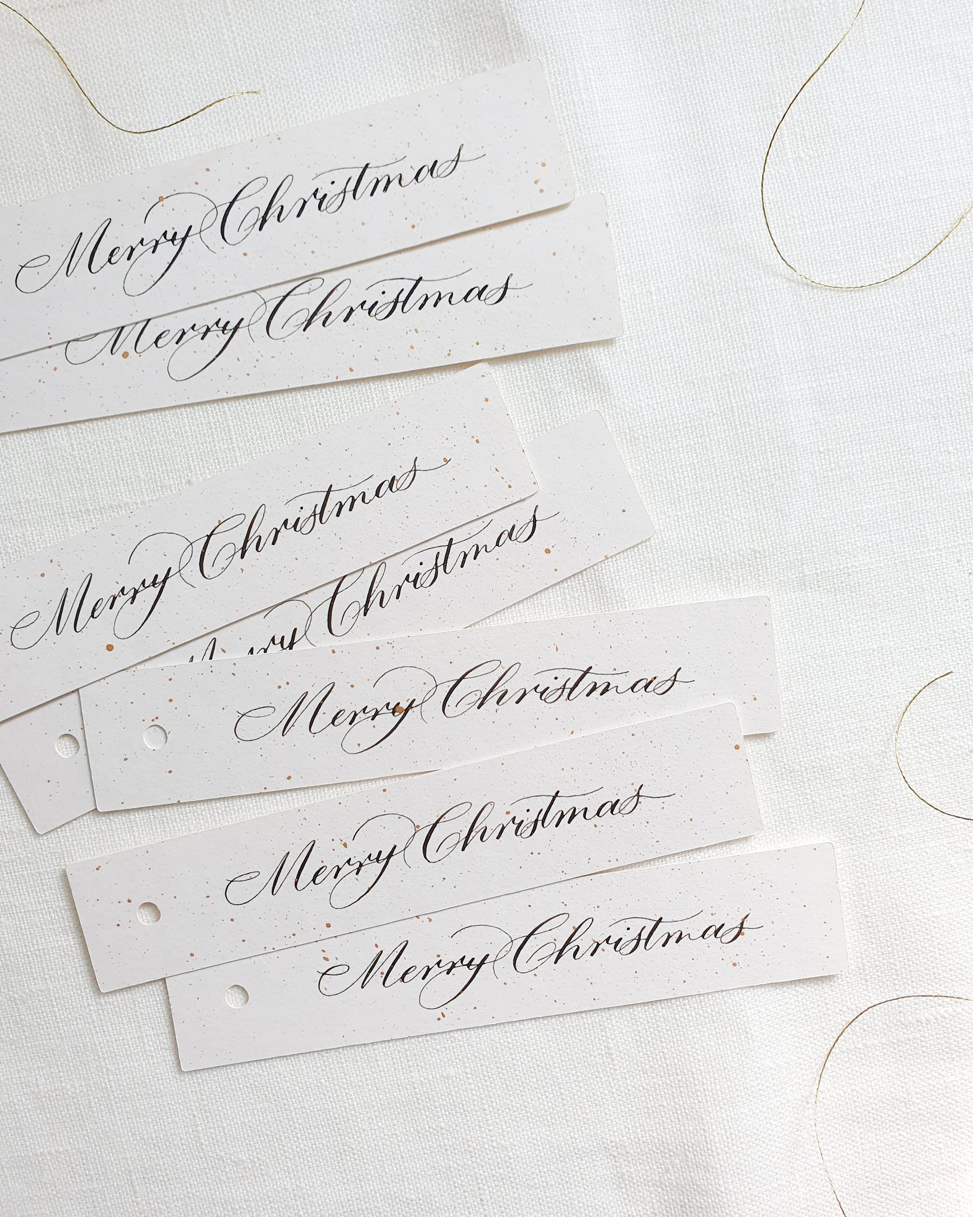 White handwritten Christmas gift tags with gold twine against a white background.