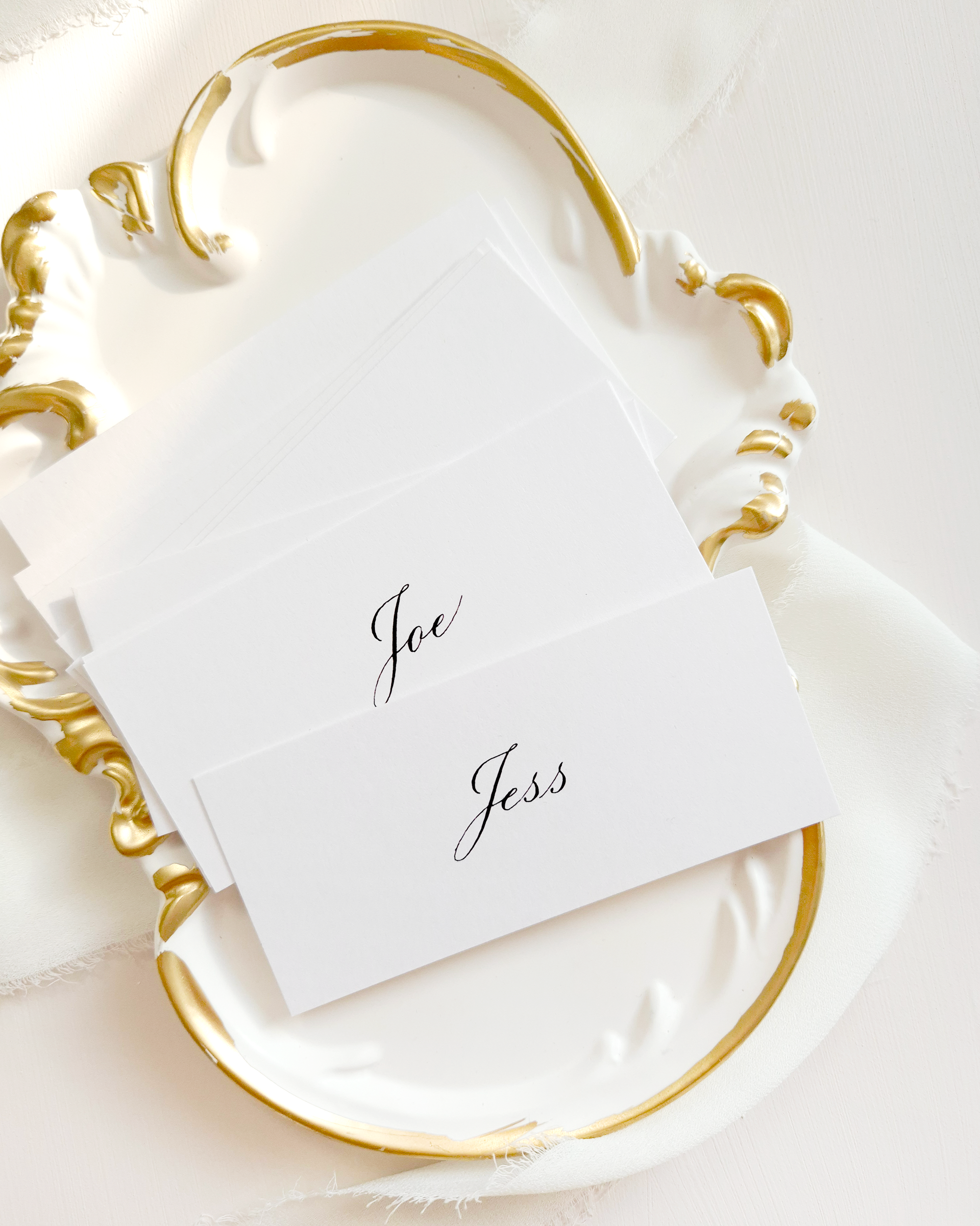 White place cards with names written in black calligraphy. The place cards are lying on an ornate plate with gold edges.