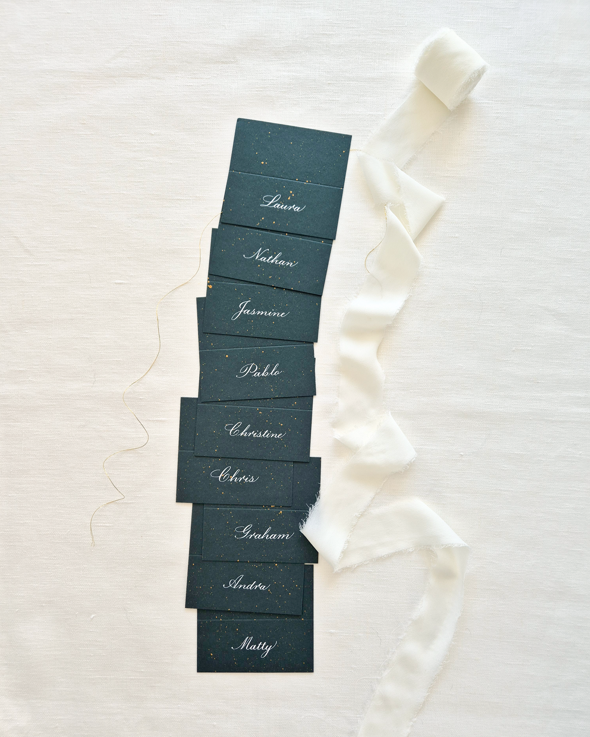 Festive green and gold place cards showing names written in copperplate calligraphy against a white background.