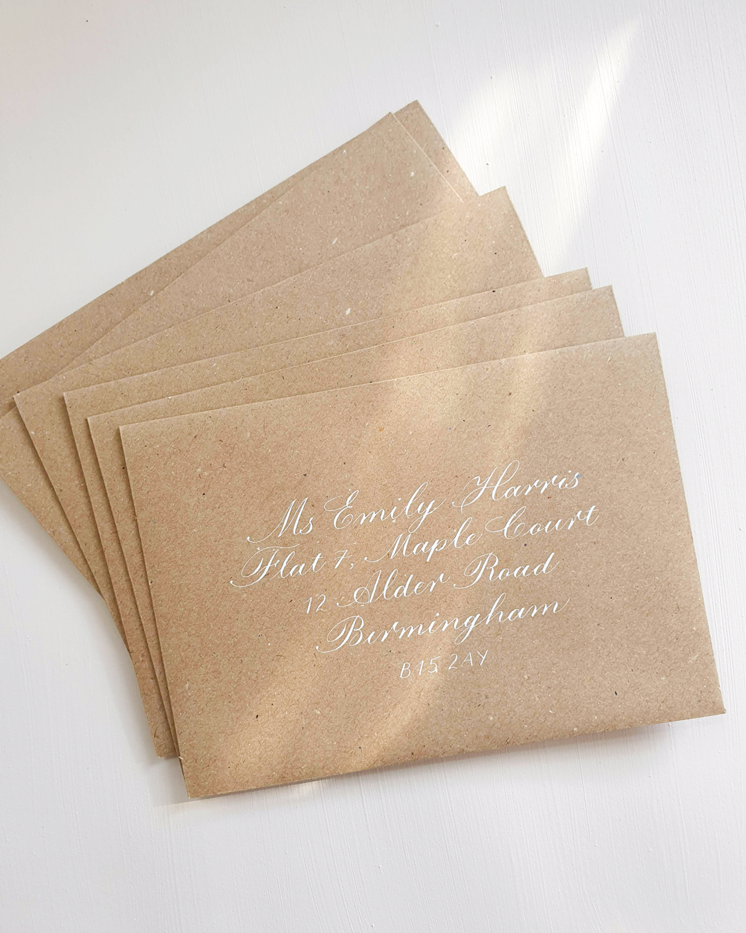 Kraft brown envelope rests on white background with address written on front in copperplate calligraphy with white ink.