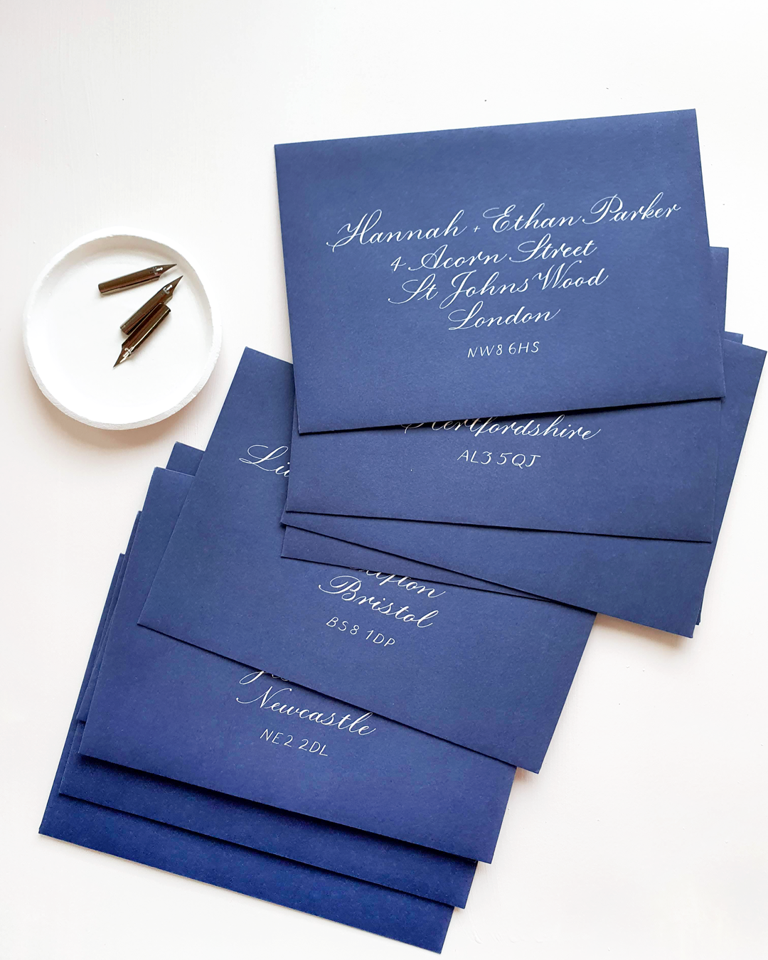Navy blue envelopes next to a white dish holding nibs for a calligraphy pen.