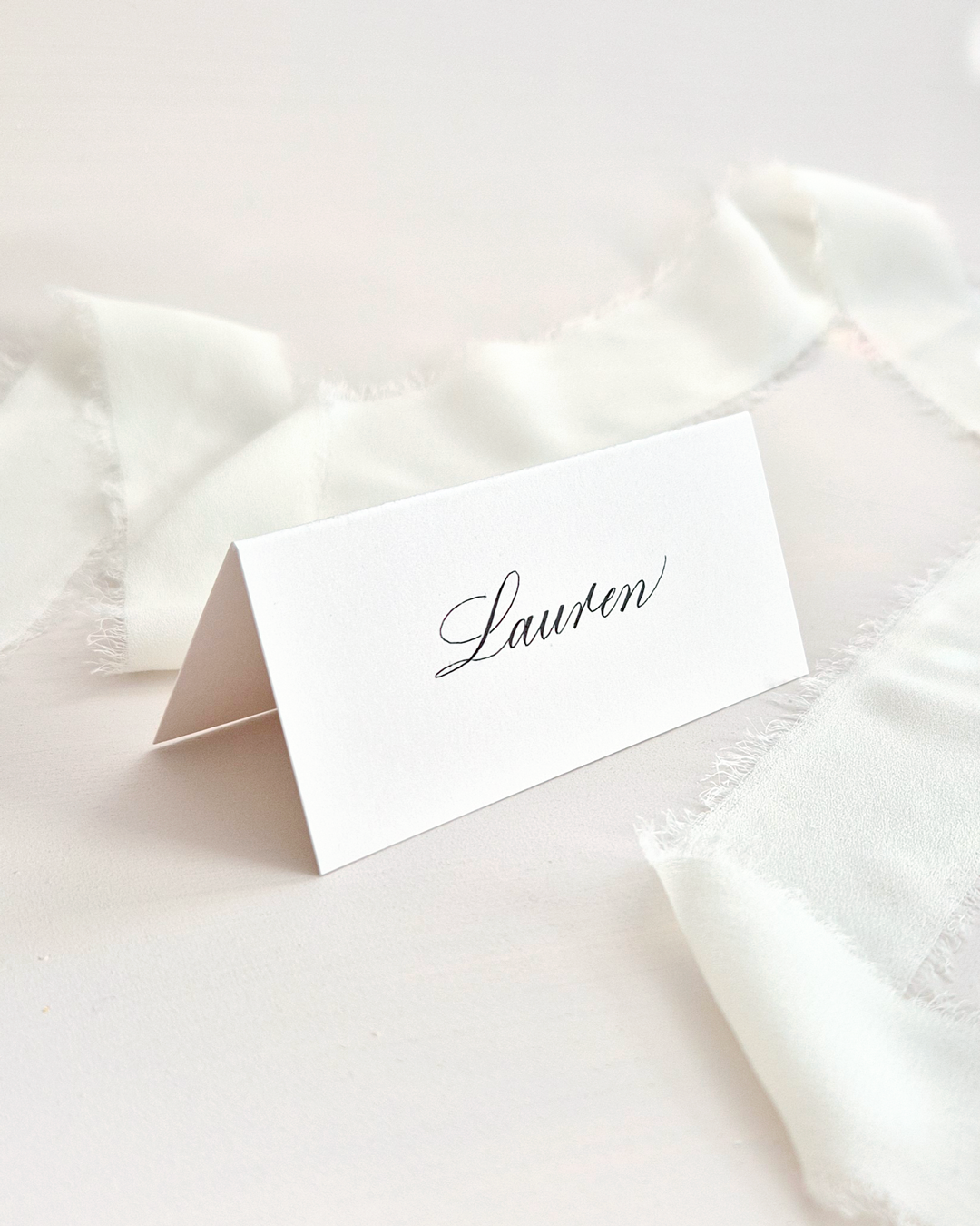 A tented place card on a neutral background. A name has been written on the place card in black ink.