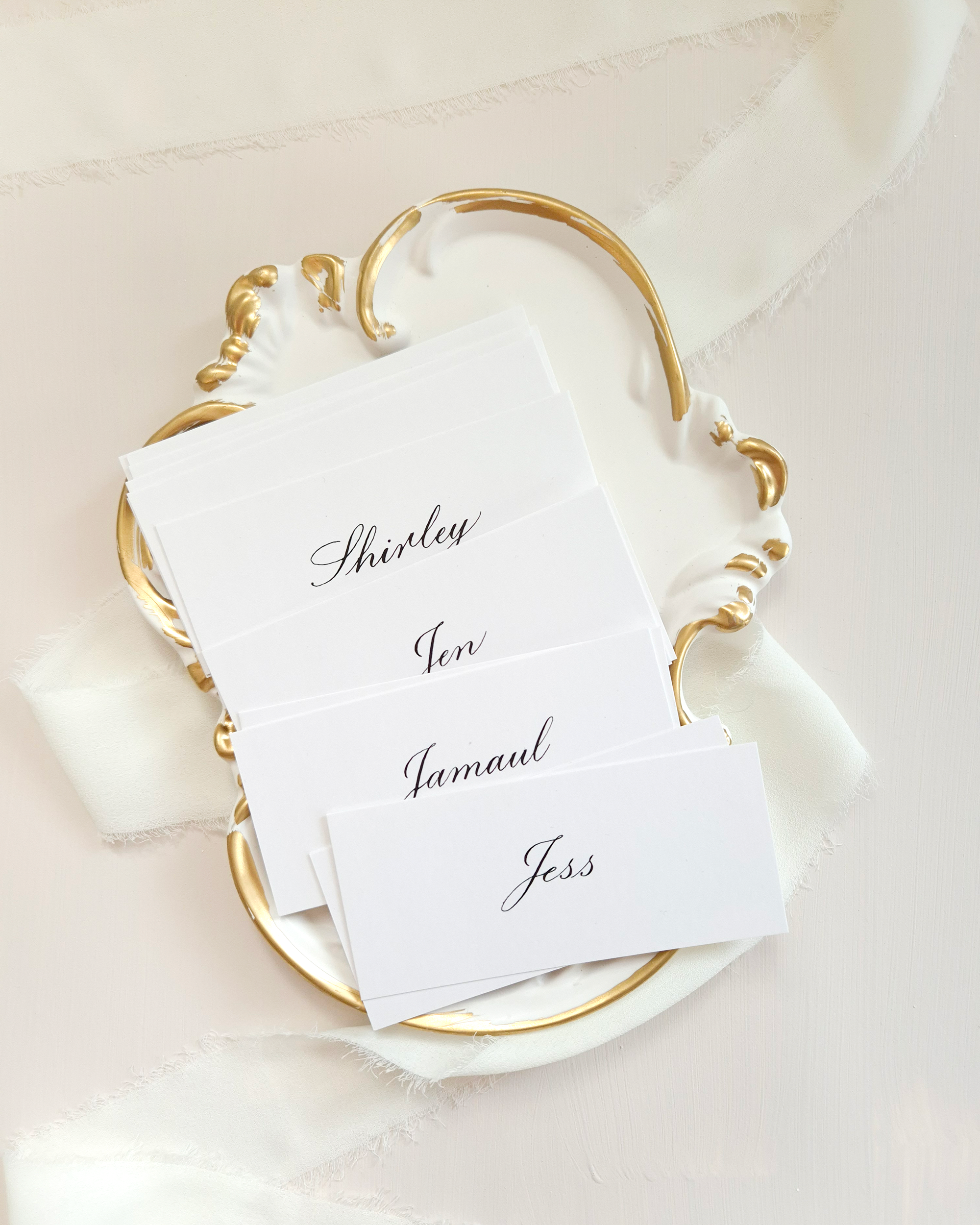 White place cards with black calligraphy names on them. The names are 'Shirley', 'Jen', 'Jamaul', and 'Jess'.