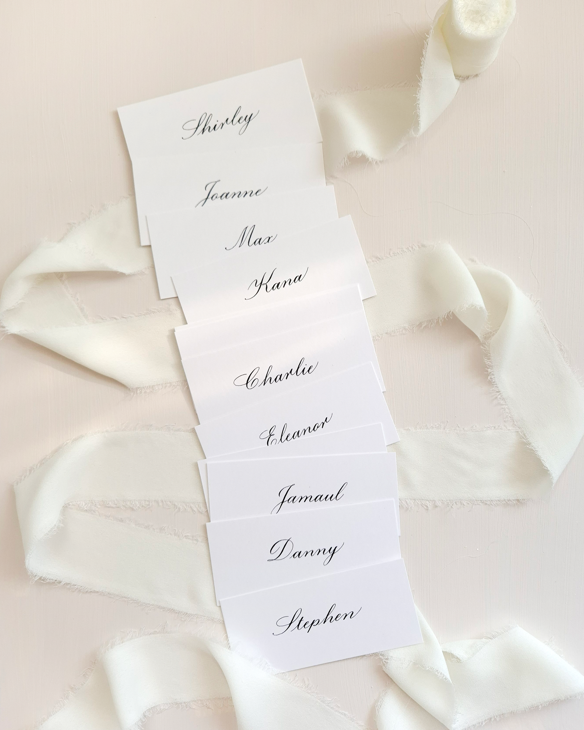 White place cards with black calligraphy names: Shirley, Joanne, Max, Hana, Charlie, Eleanor, Jamaul, Danny, Stephen.