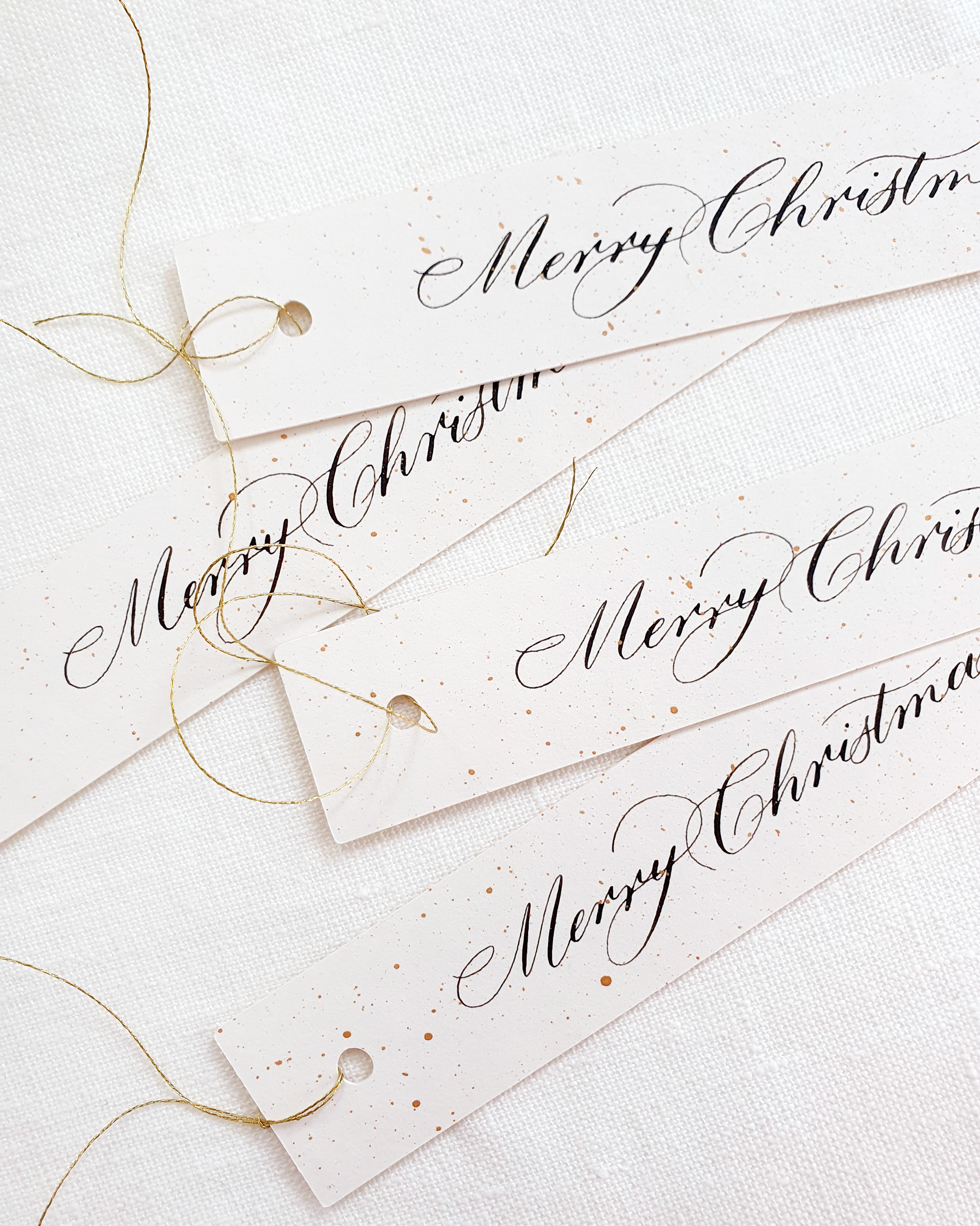 White handwritten Christmas gift tags with gold twine against a white background.