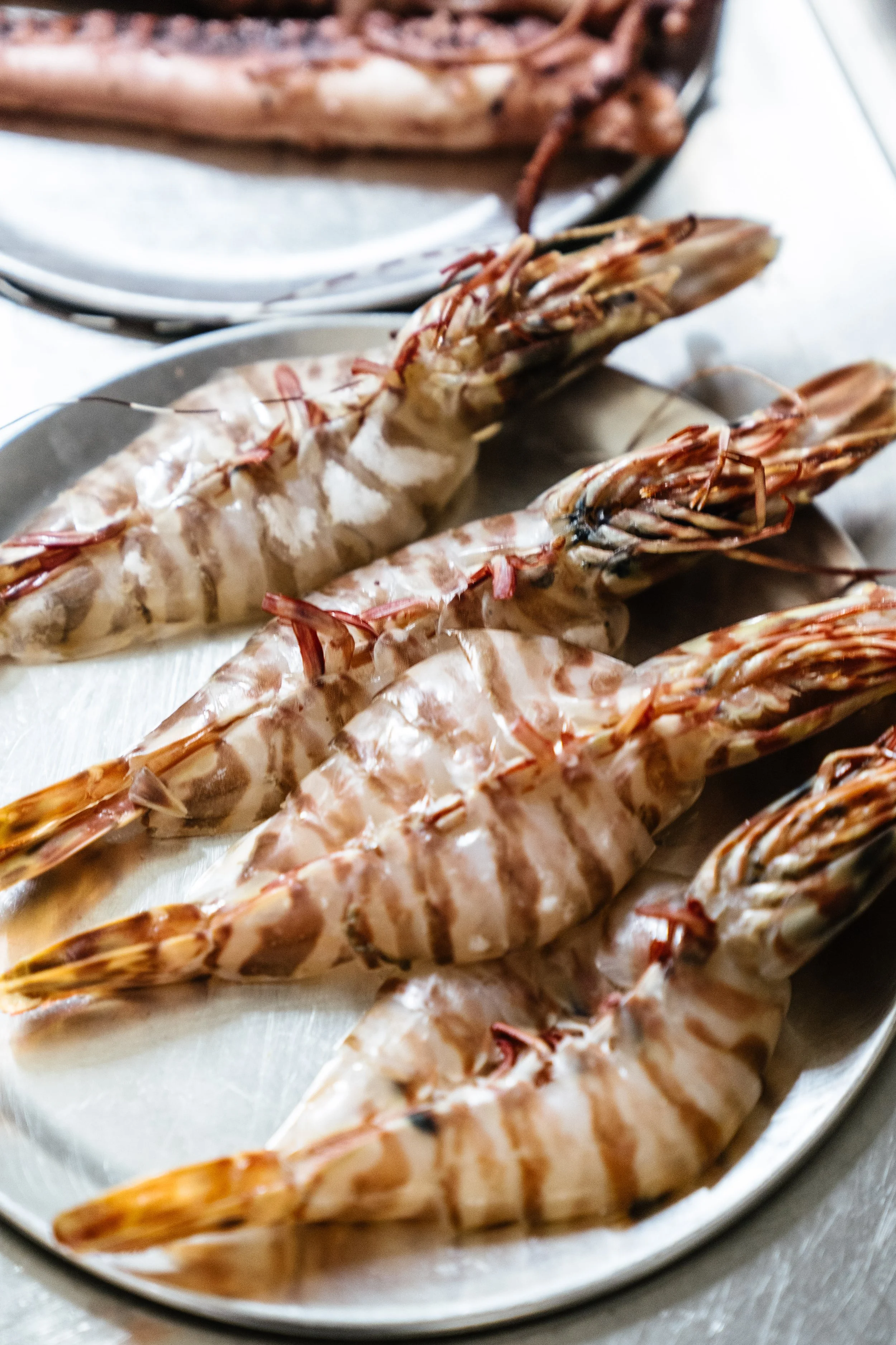 Raw shrimp on a platter with a second plate of cooked shrimp in the background.