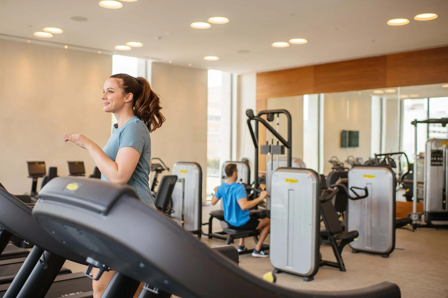 A woman running on a treadmill in a gym with two children using exercise equipment in the background.