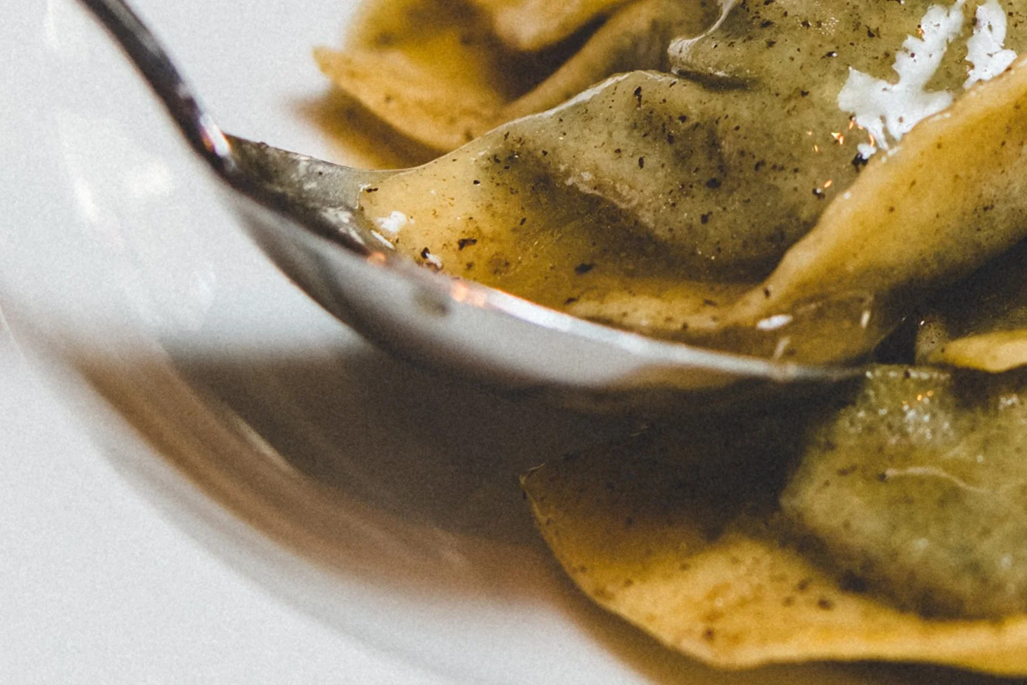 Close-up of fried tortellini pasta with melted cheese and herbs on a silver spoon.
