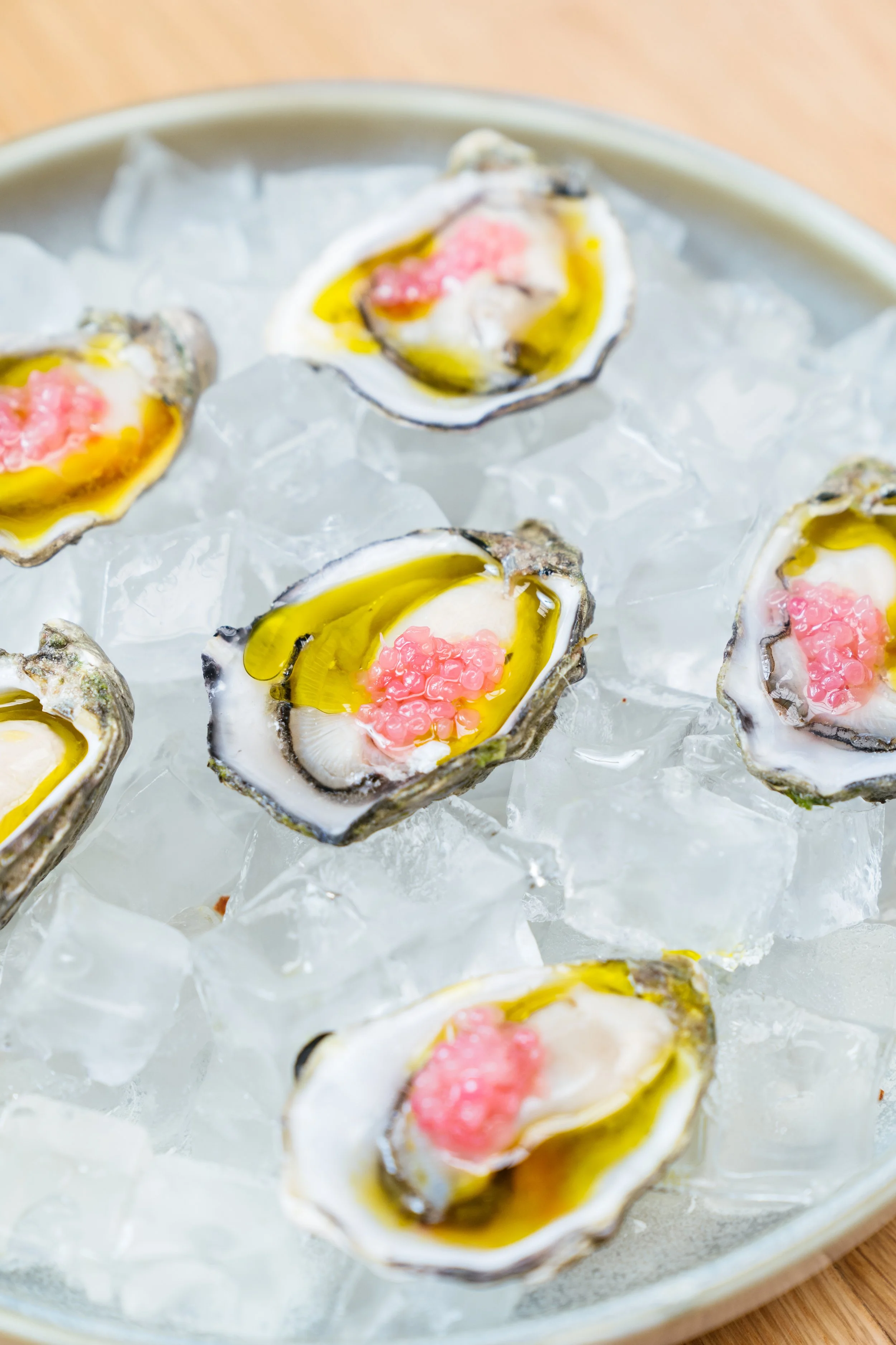 Fresh oysters on a bed of ice, topped with pink fish roe and drizzled with yellow sauce.