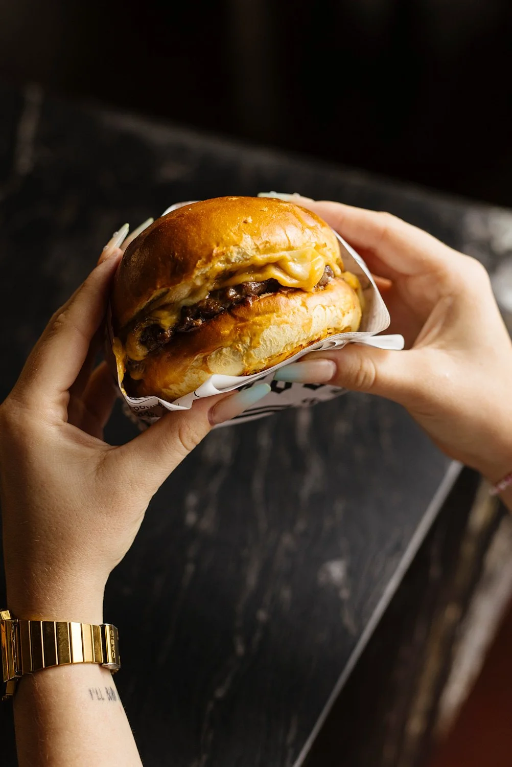 Person holding a cheeseburger in a paper wrapper.
