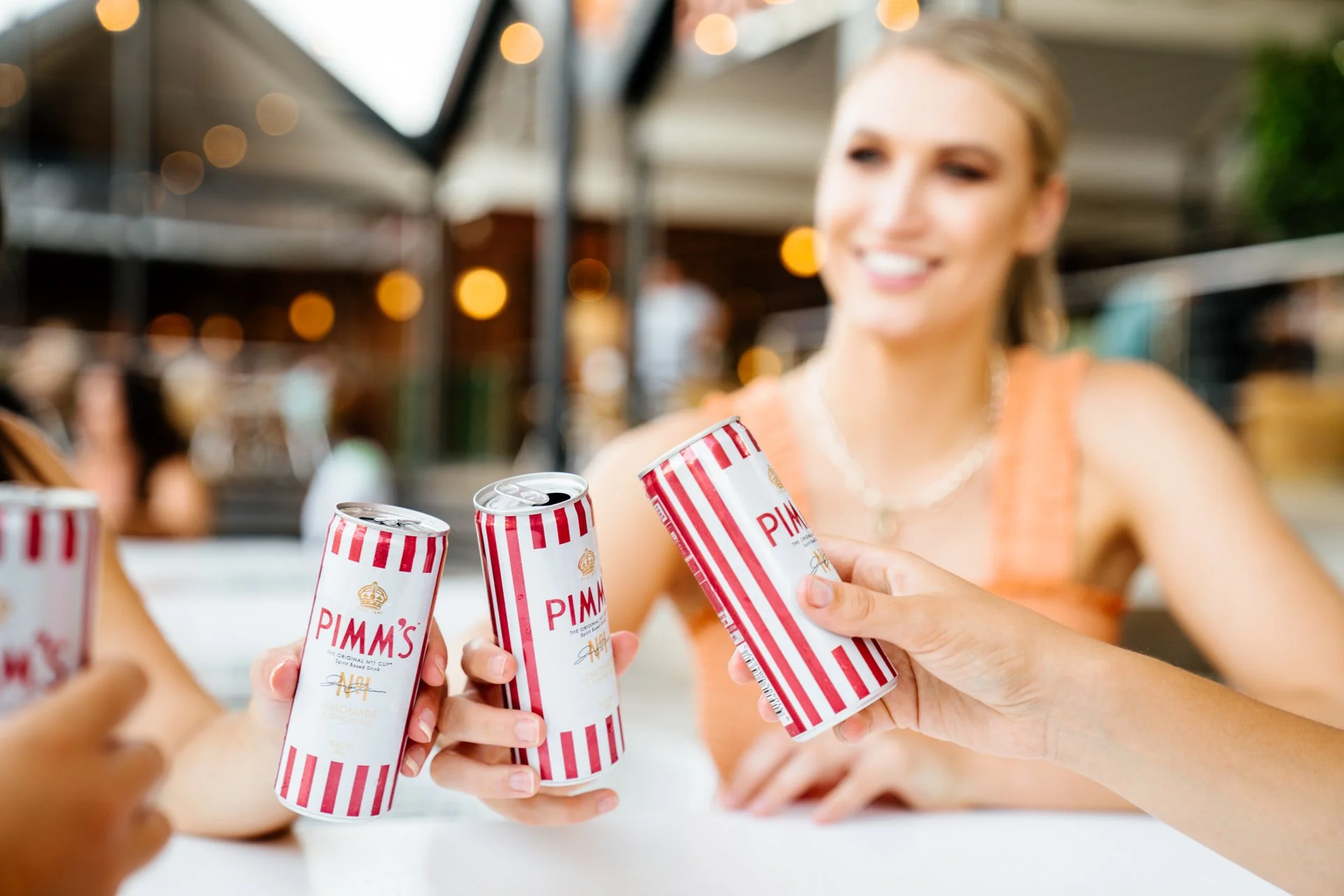 Group of people toasting with cans of Pimm's at an outdoor gathering, smiling and enjoying the moment.