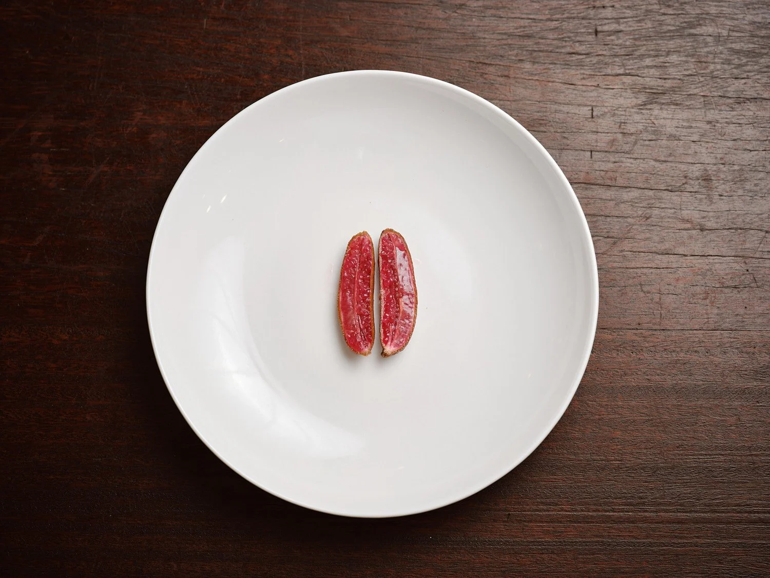 Two slices of pink grapefruit on a white plate placed on a wooden table.
