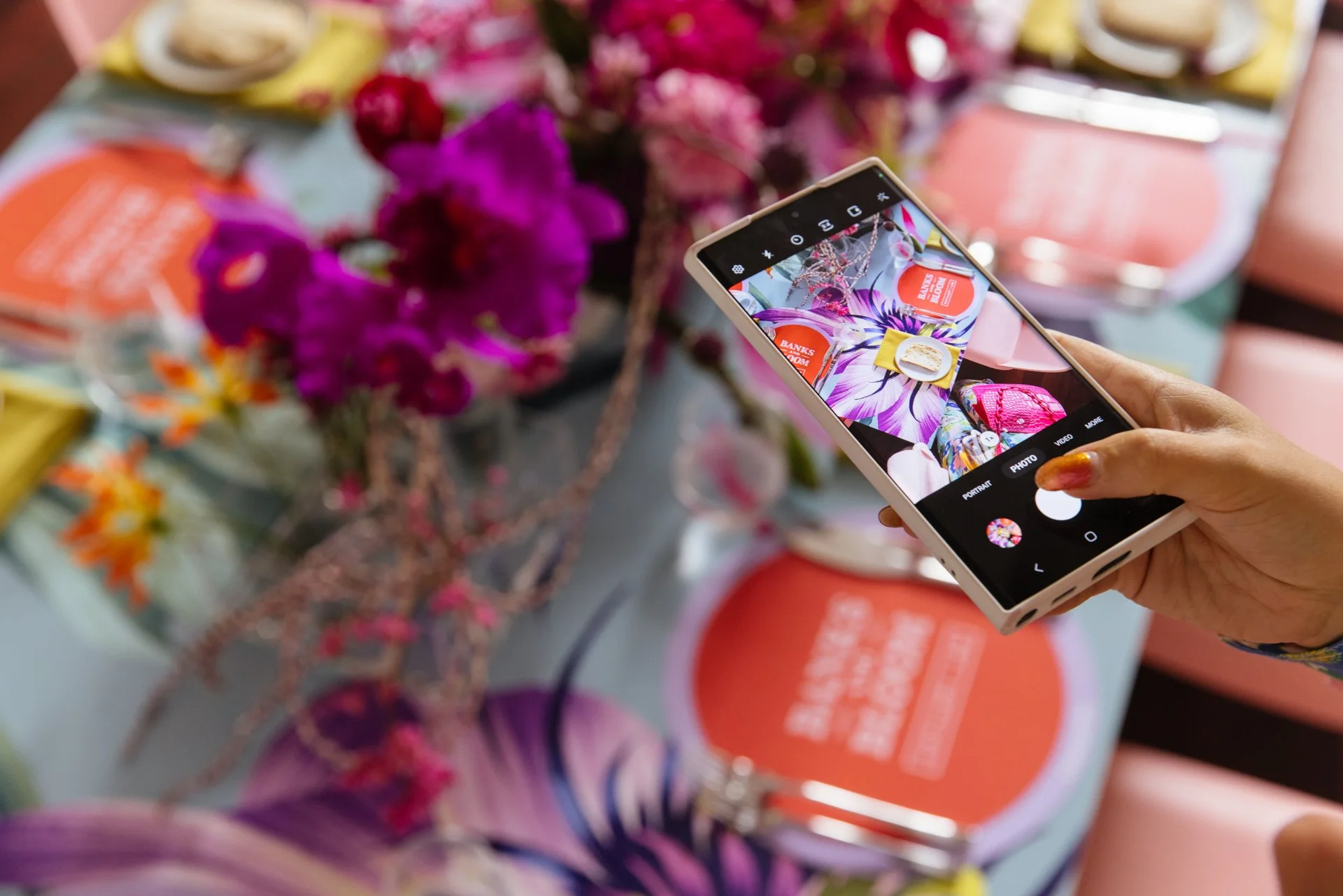 A person taking a photo of a floral arrangement on a table with a smartphone.