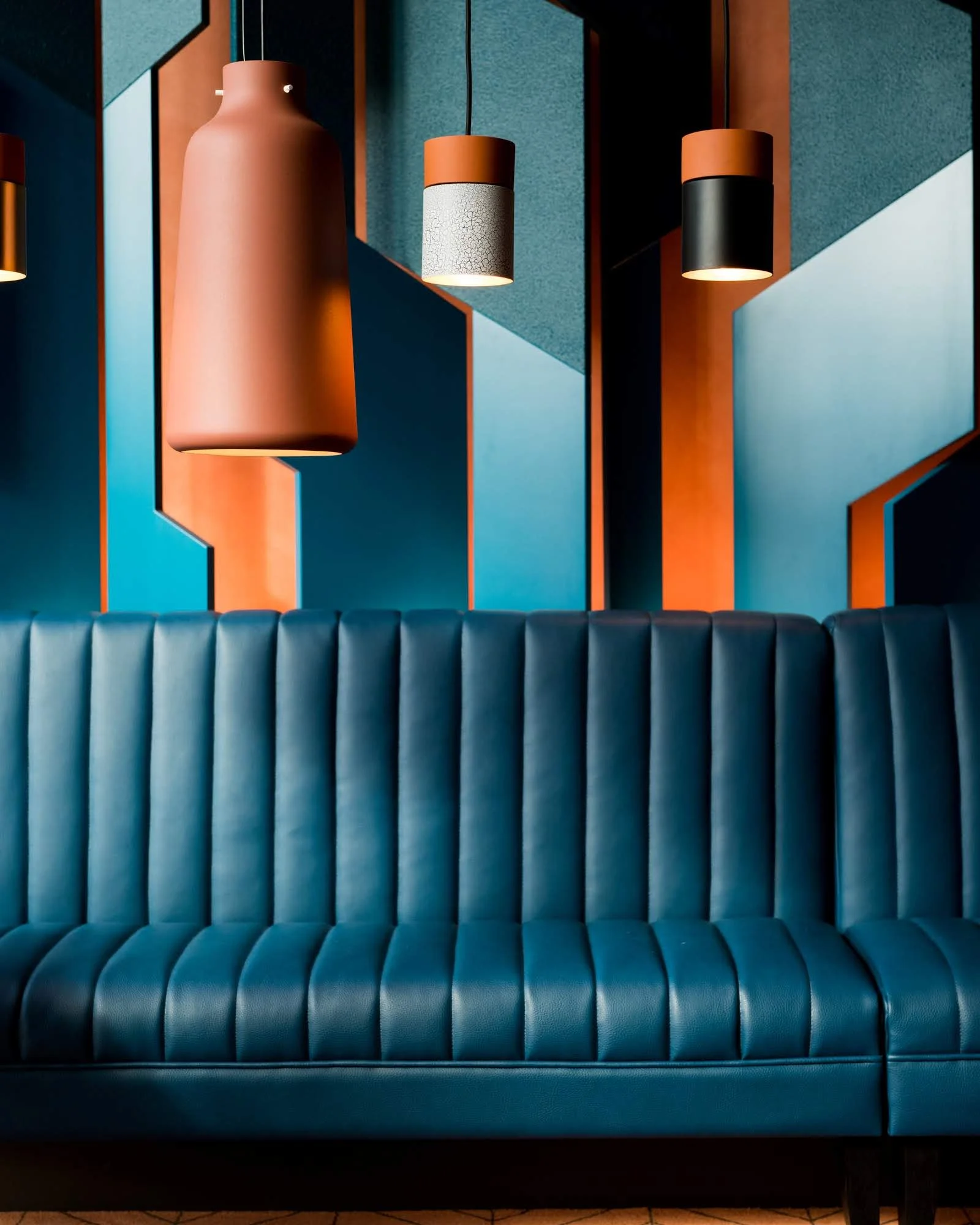 Modern interior with a blue, ribbed sofa, hanging pendant lights, and geometric wall art in shades of blue, black, and orange.