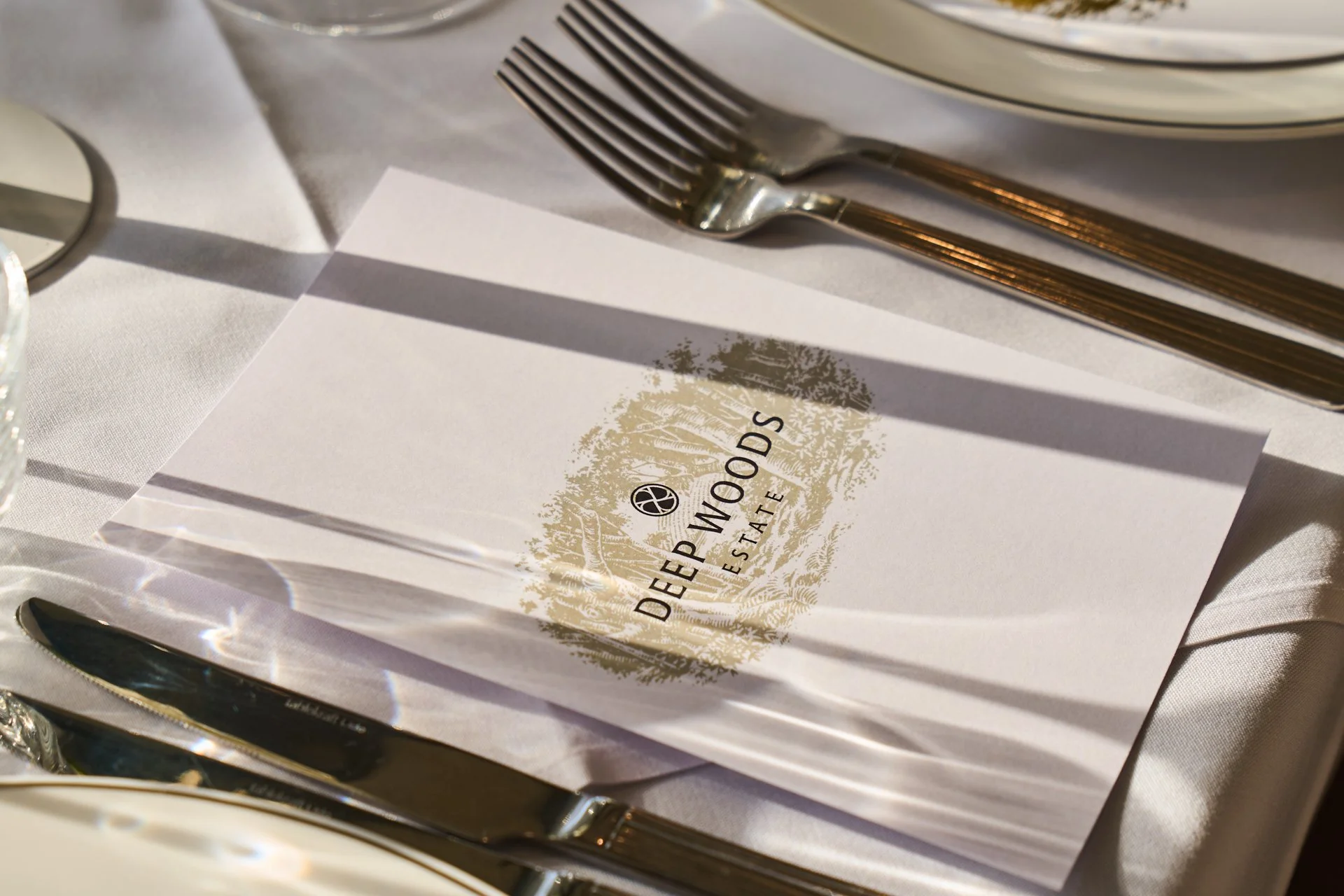 A white place setting with a Deep Woods Estate menu card, a fork and knife, on a white tablecloth.